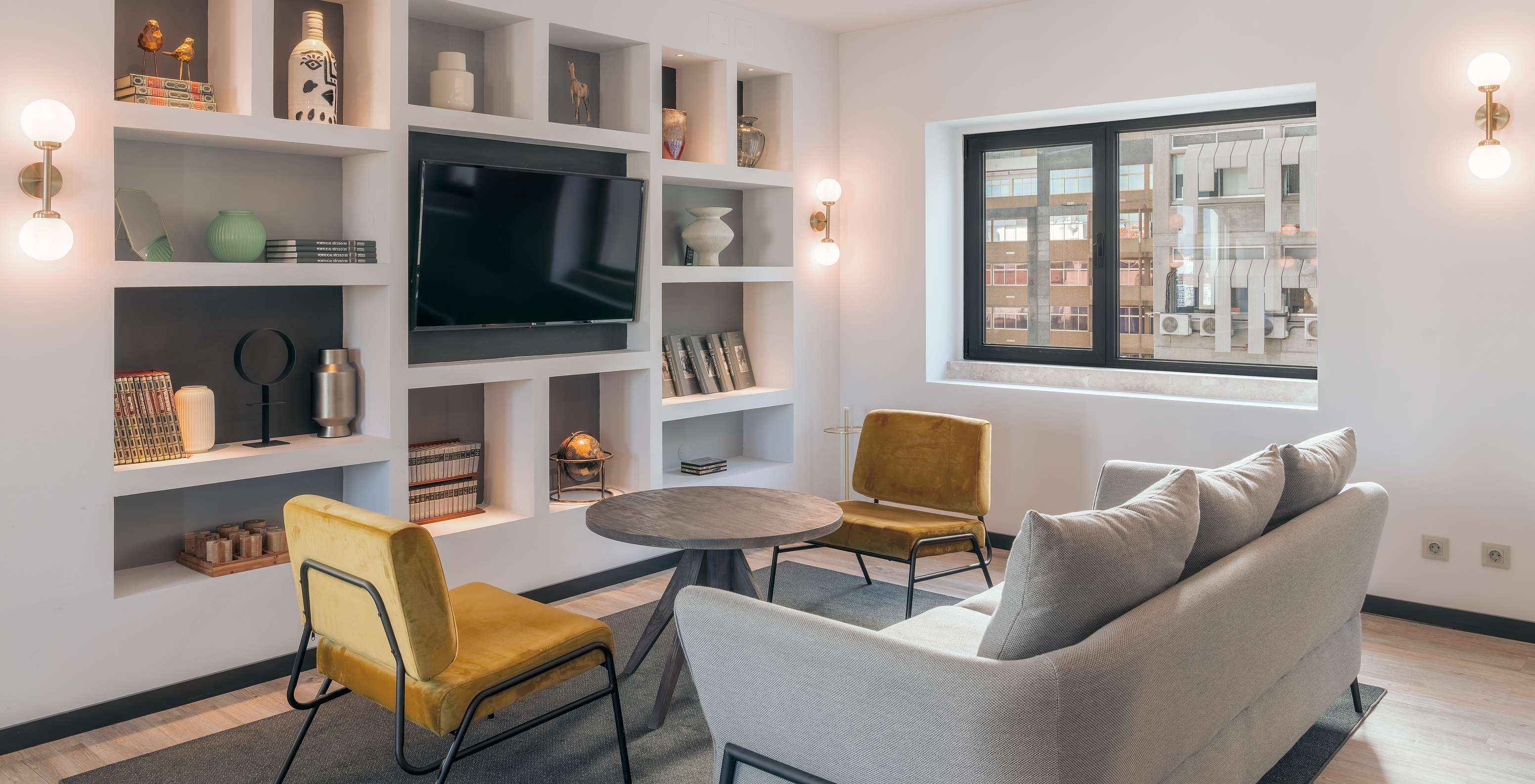 Lounge avec canapé chaises table basse télévision tapis et objets de décoration avec fenêtres donnant sur la ville