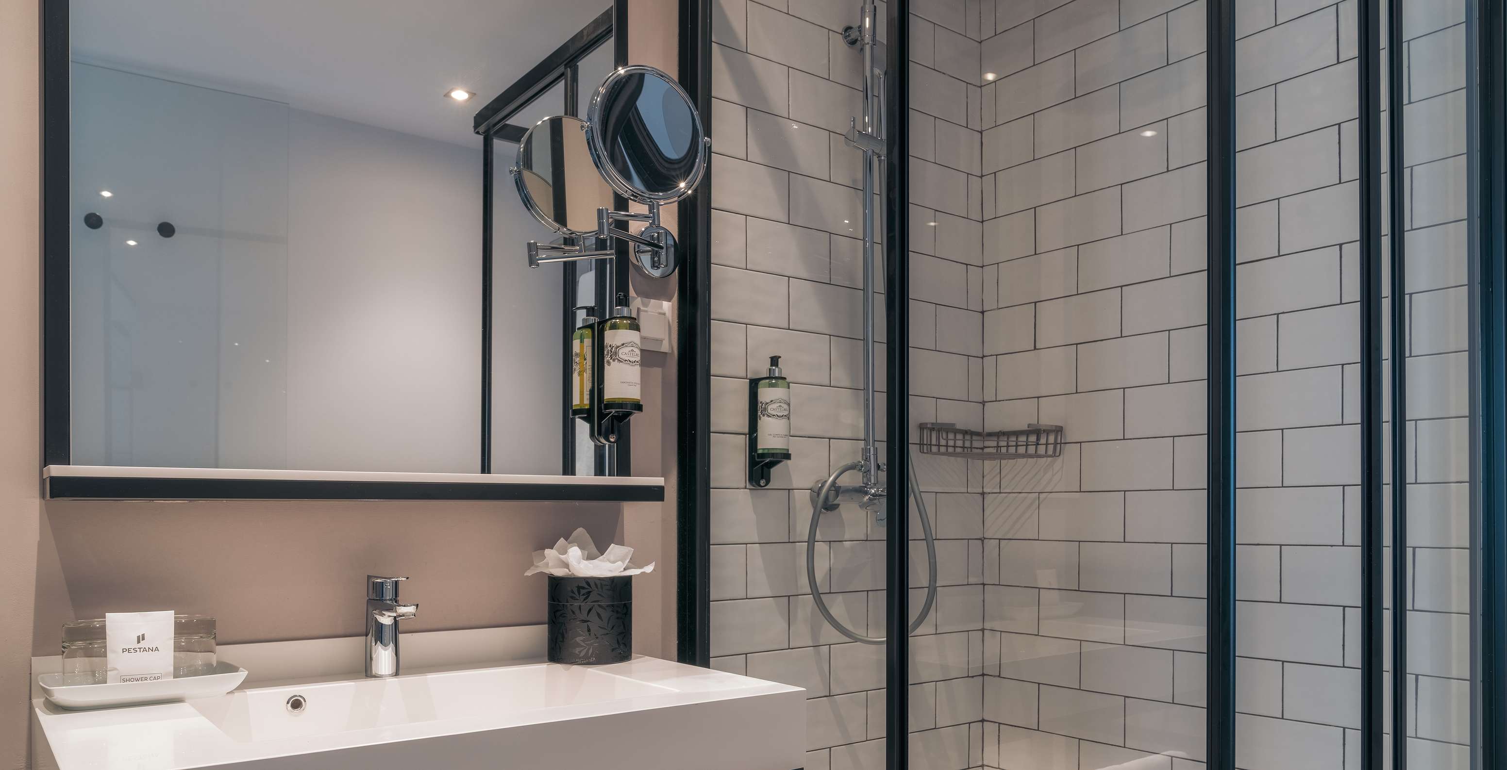 Le Vintage du Pestana Lisboa Vintage a une douche avec portes en verre et détails noirs et un lavabo avec deux miroirs