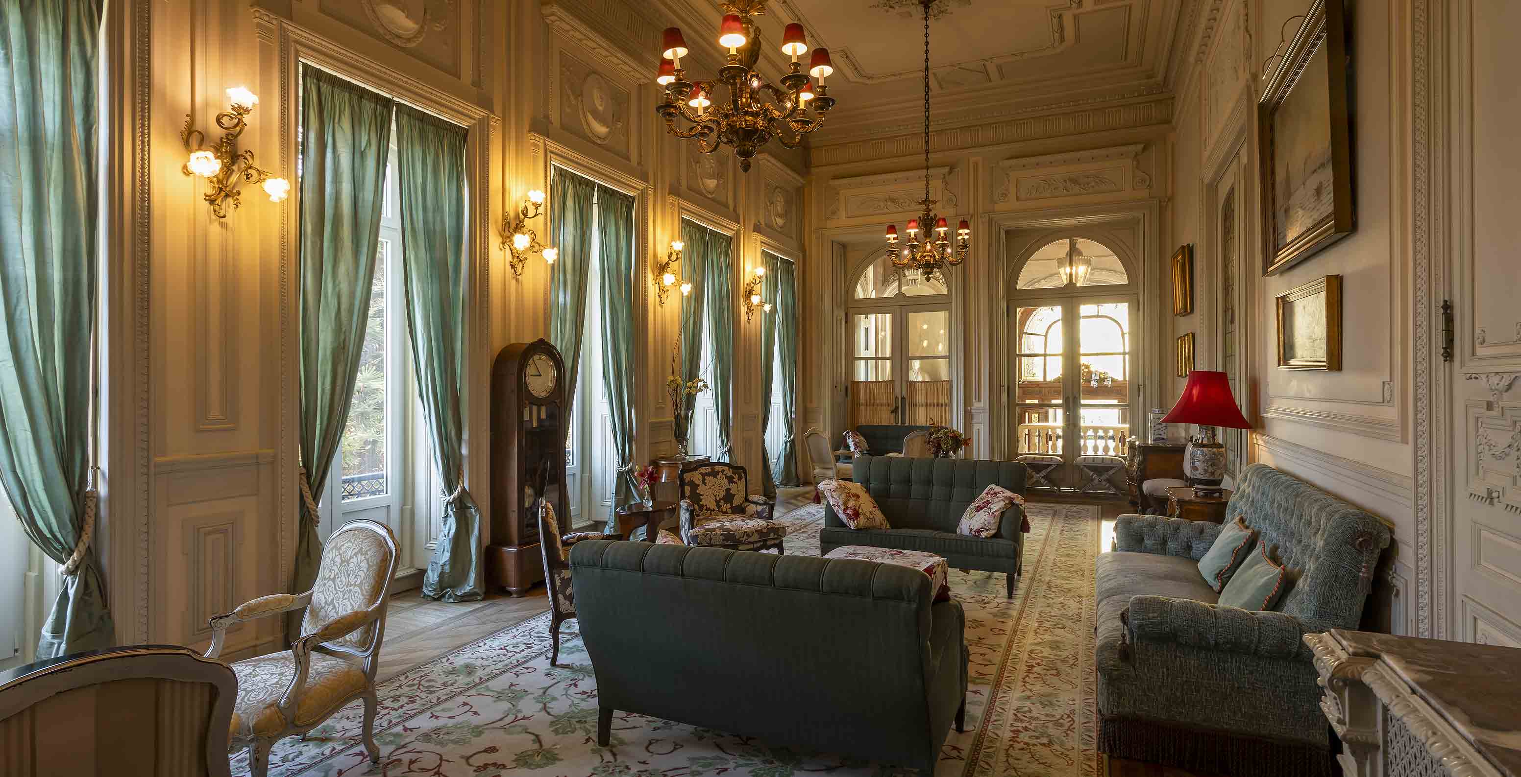 Le Pestana Palace Lisboa possède un salon avec des canapés, des fauteuils et de longues rideaux verts aux fenêtres