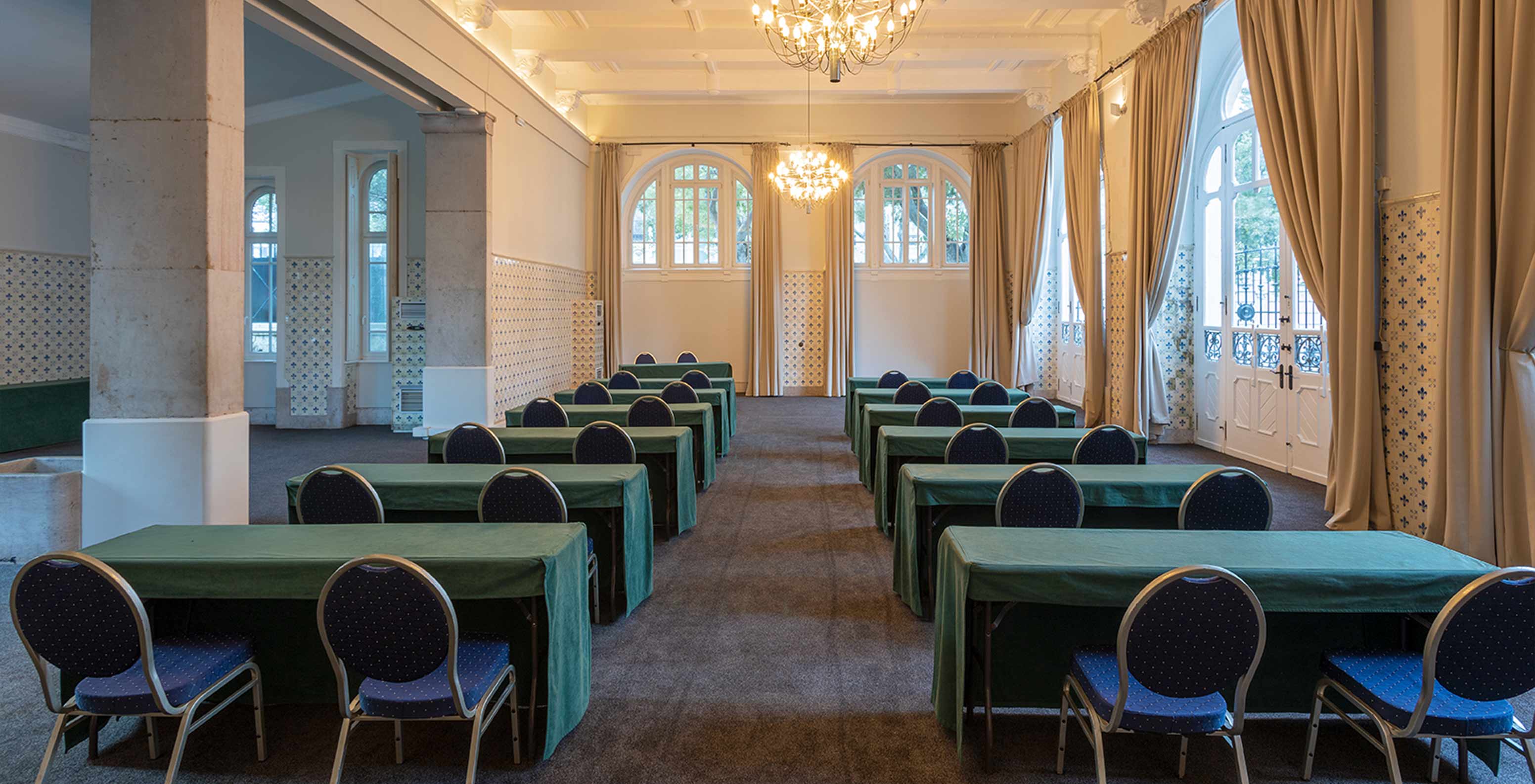 Le Pestana Palace dispose d'une salle de réunion avec de longues tables vertes, des chaises bleues et plusieurs fenêtres