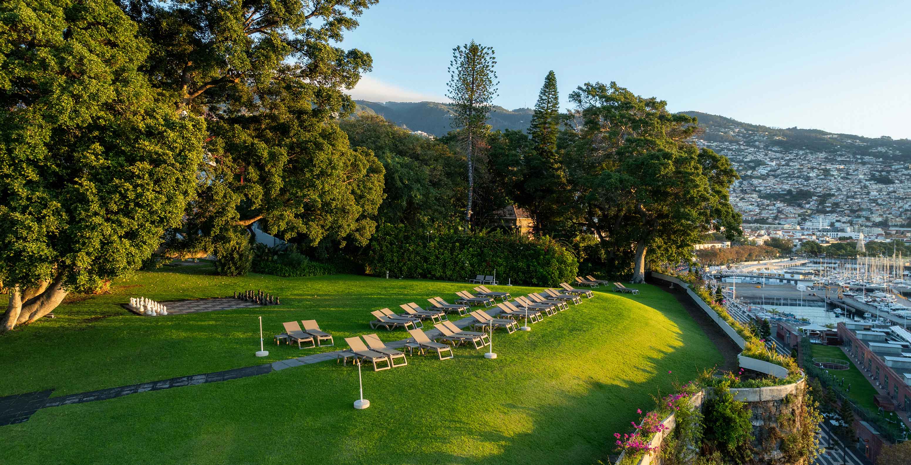 Vue du jardin du Pestana Casino Park au coucher du soleil, avec une ville en arrière-plan et un bateau de croisière ancré dans la mer.