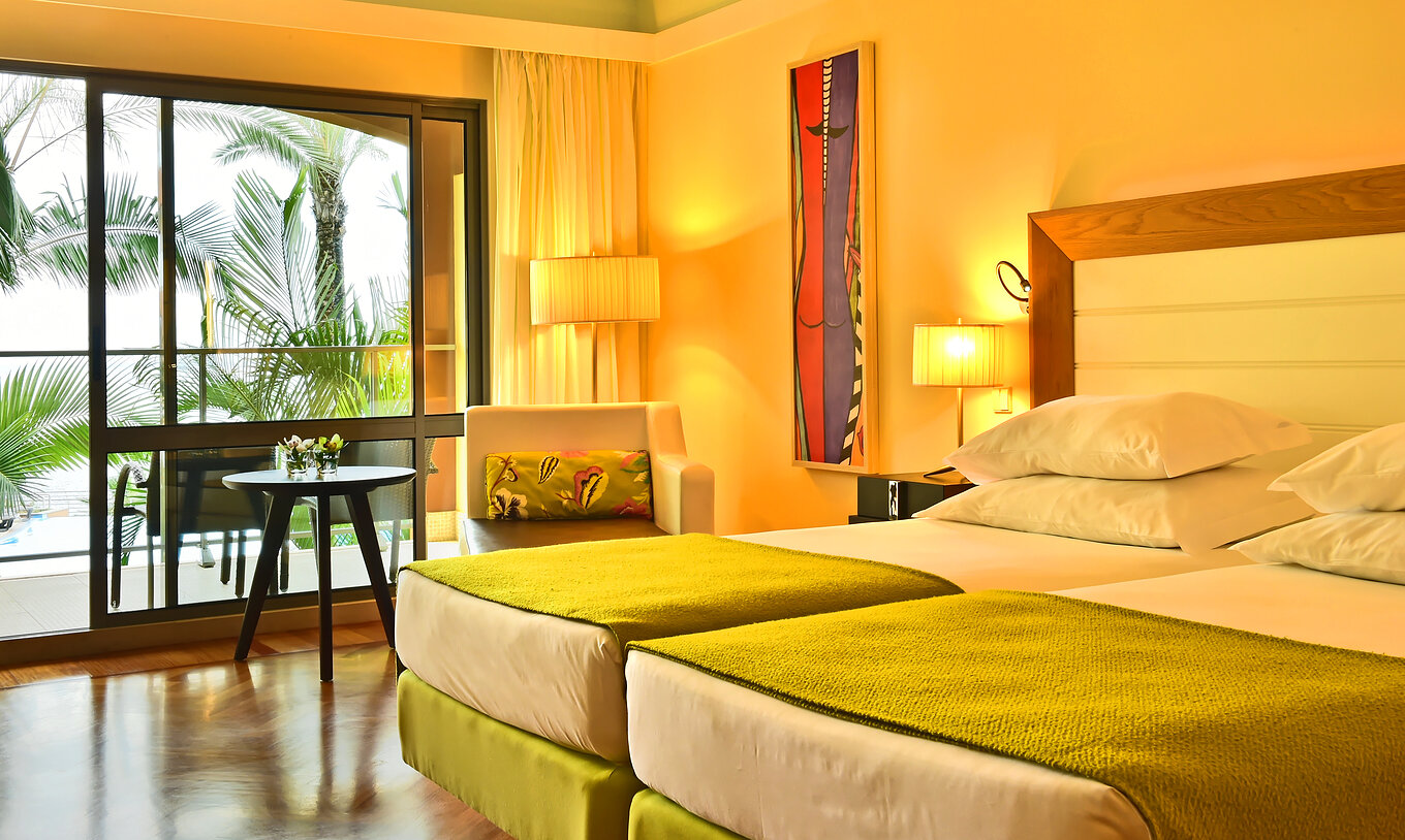 Le Classique Vue Piscine du Pestana Promenade a deux lits avec une couverture verte et une grande fenêtre pour le balcon