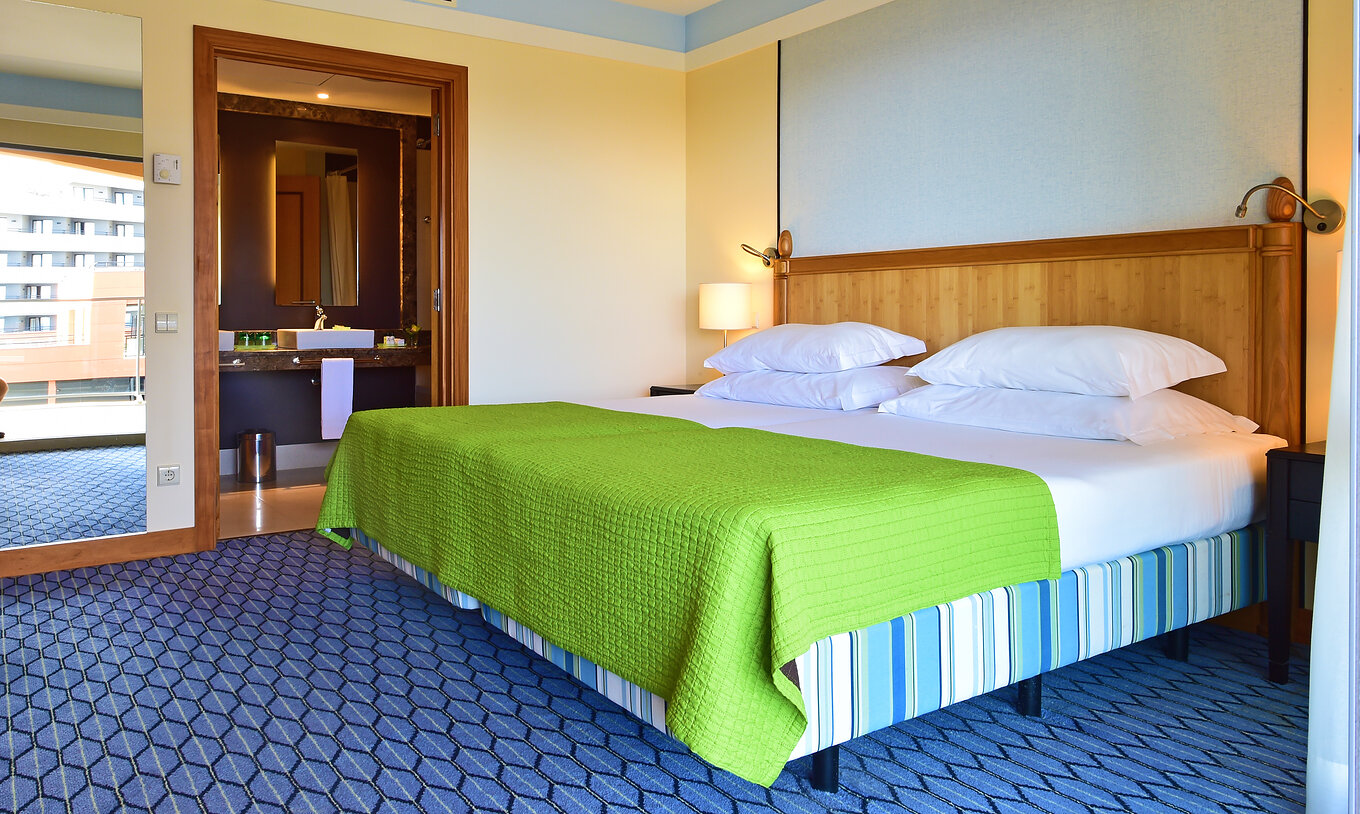 La Suite du Pestana Promenade a un lit double avec une couverture verte, un grand miroir et une salle de bain