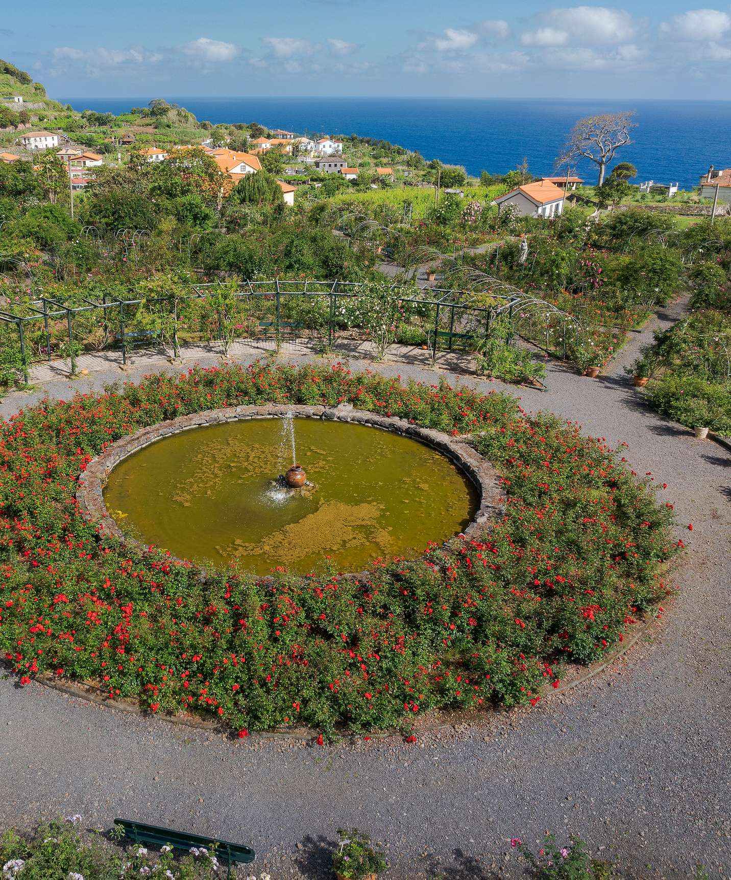 Vue du rosier de la Quinta do Arco avec la fontaine au centre, entourée de diverses fleurs et vue sur la mer