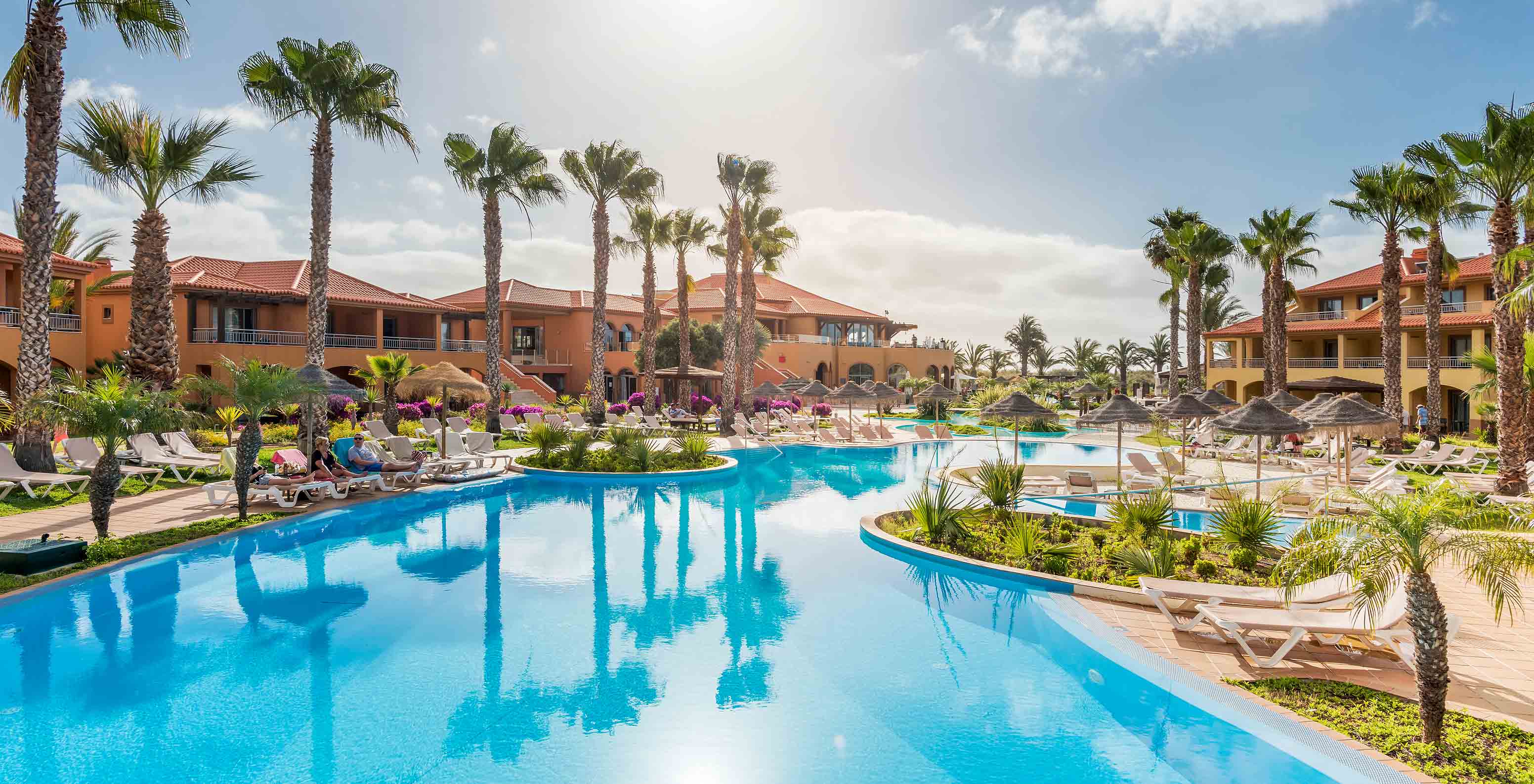 Grande piscine bleue Pestana Porto Santo, transats, palmiers, bâtiments sous ciel ensoleillé
