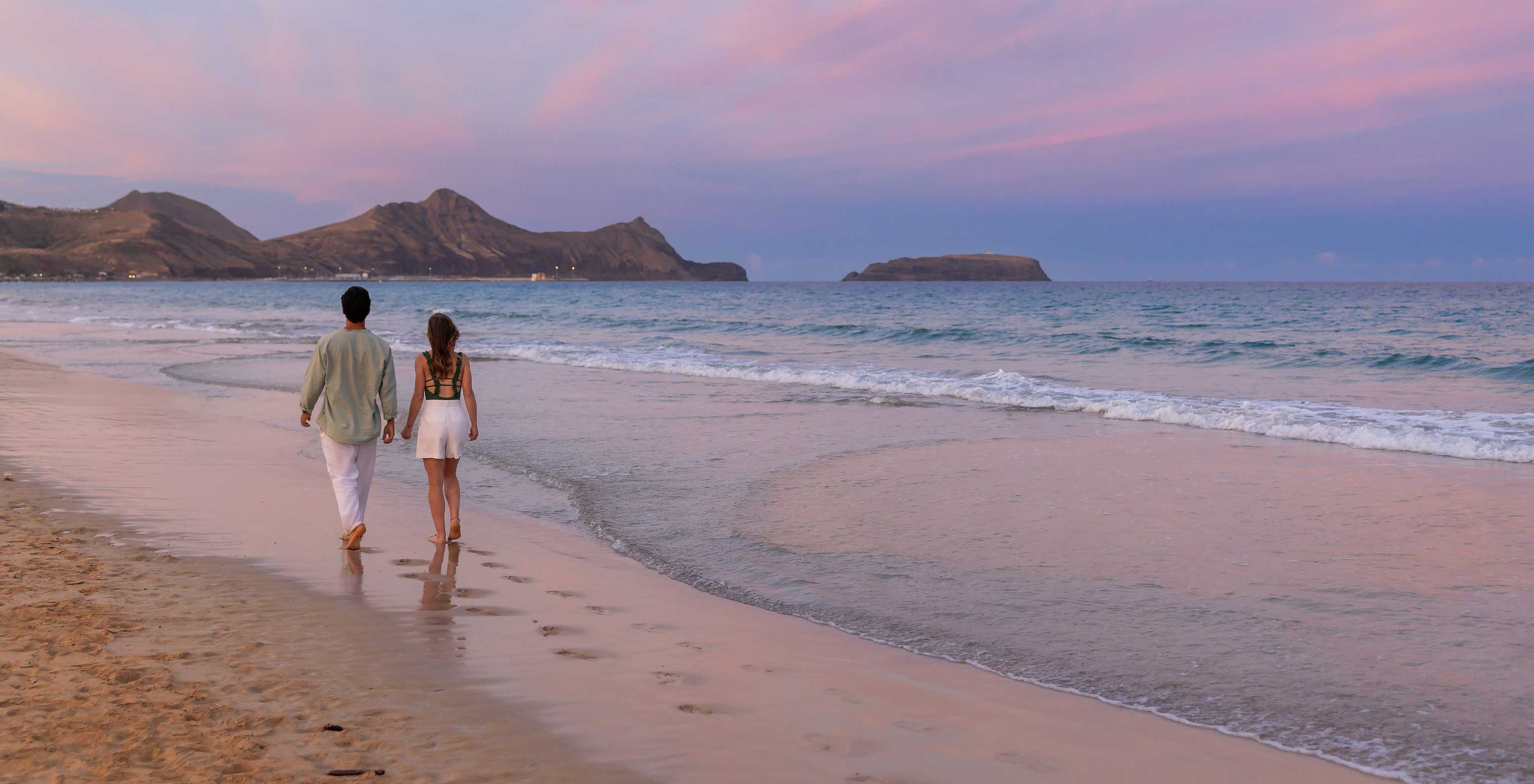 Un couple se promenant au bord de la mer sur la plage de l’île de Porto Santo, en face du Pestana Porto Santo All Inclusive