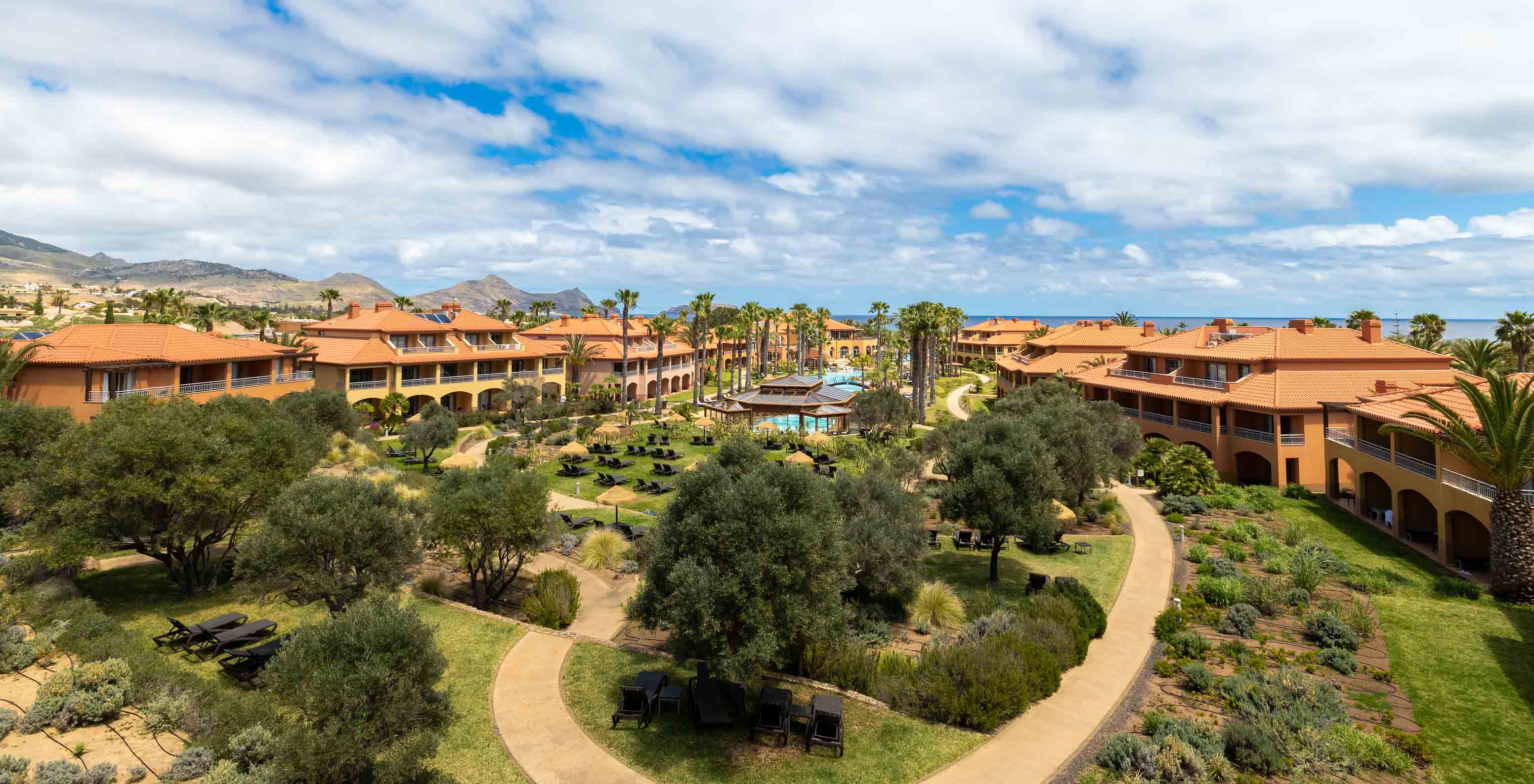 Jardins du Pestana Porto Santo All Inclusive avec pelouse, palmiers tropicaux, chaises longues et villas tout autour
