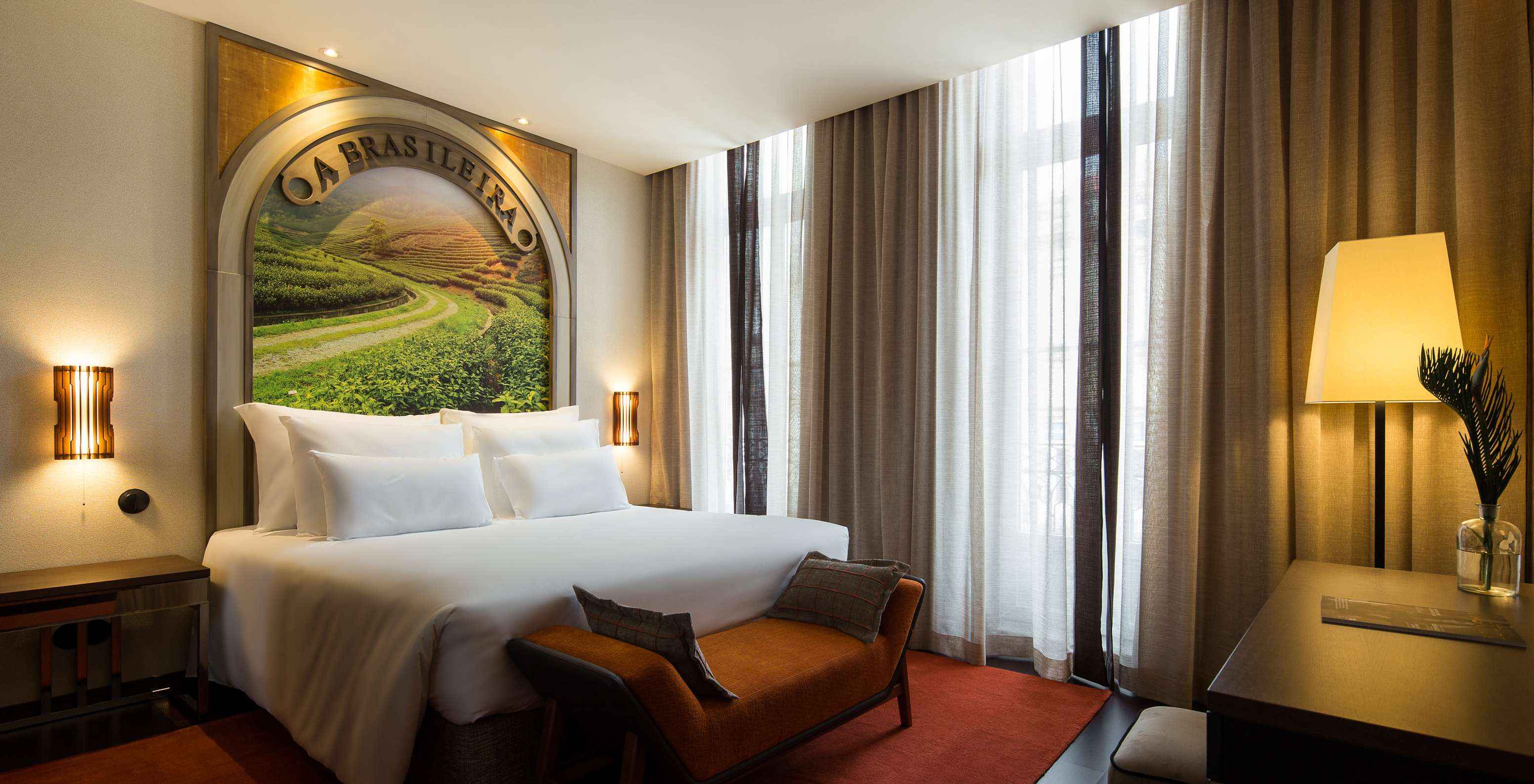 Le Deluxe Supérieur du Pestana Porto - A Brasileira a un lit avec fresque thématique sur la tête de lit et un banc au fond.