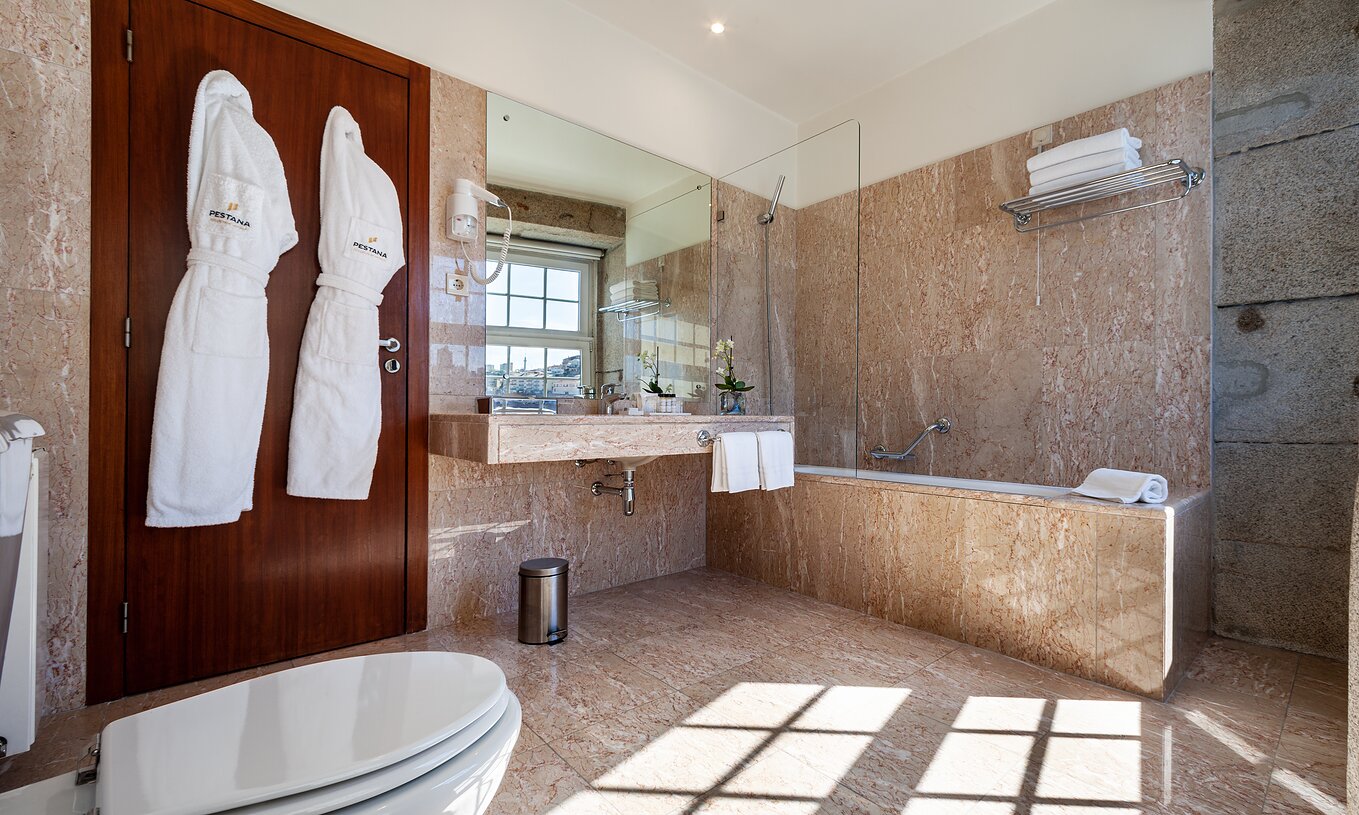 Le Plaza du Pestana Vintage Porto a une salle de bain avec baignoire, deux peignoirs, lavabo et sèche-cheveux