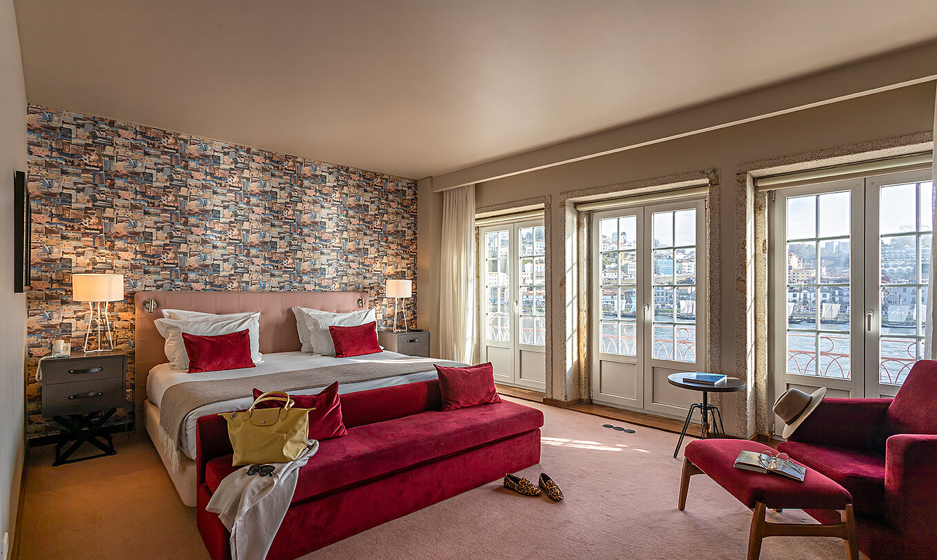 La Suite Grand View du Pestana Vintage Porto dispose d'un lit double, d'un canapé rouge et de fenêtres avec vue sur Porto