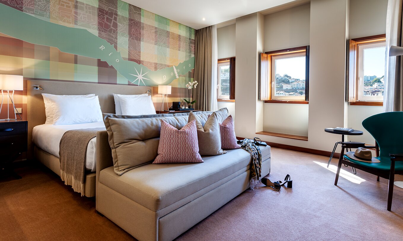 Le Vintage Front View du Pestana Vintage Porto a un lit double avec un canapé aux pieds, trois fenêtres et un fauteuil