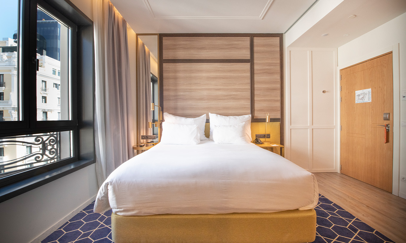 Le Premium avec Vue du Pestana CR7 Gran Vía Madrid a un lit double et une grande fenêtre avec vue sur les bâtiments en face