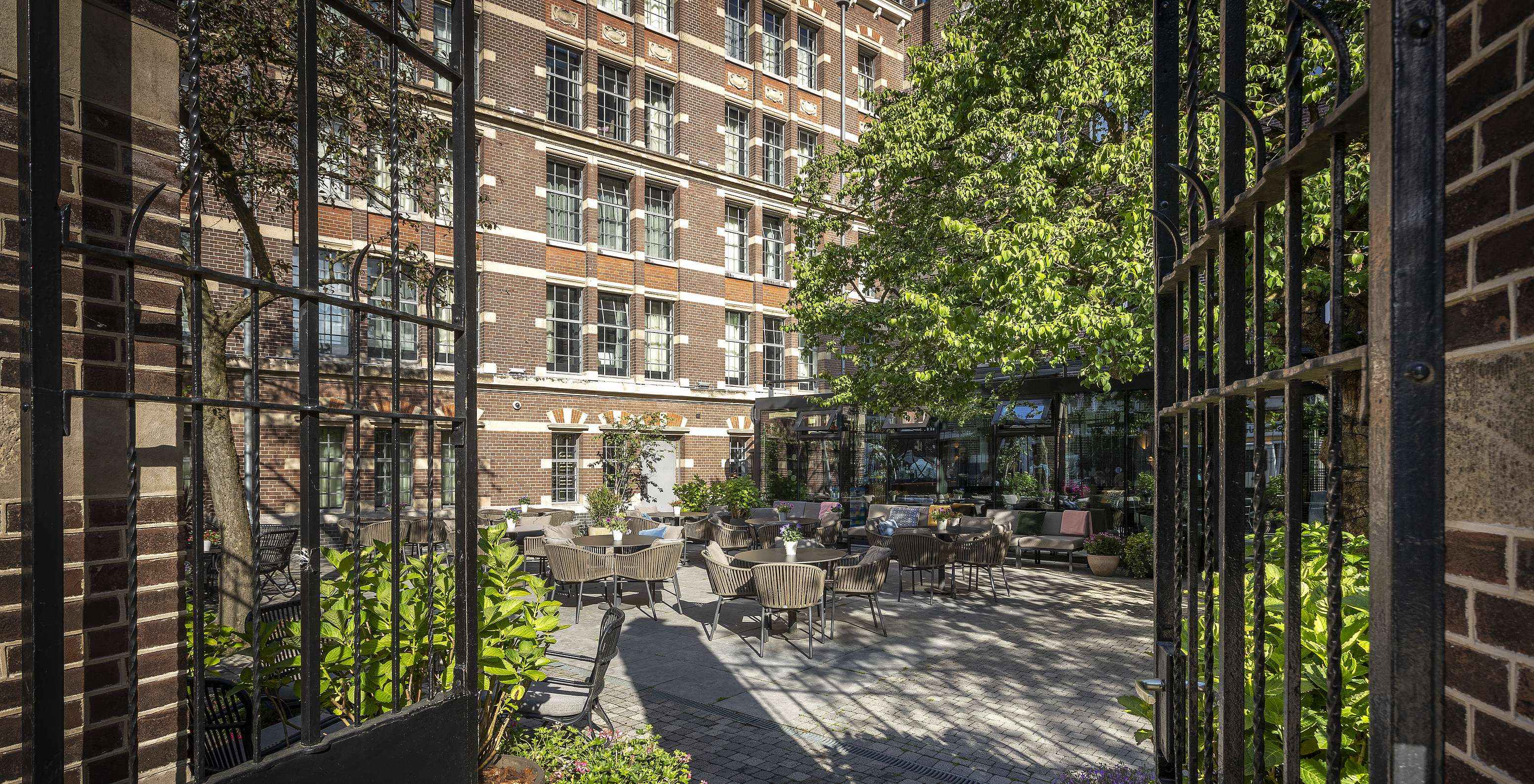 Terrasse du Pestana Amsterdam Riverside, avec des tables rondes et des chaises, avec la façade de l'hôtel en arrière-plan