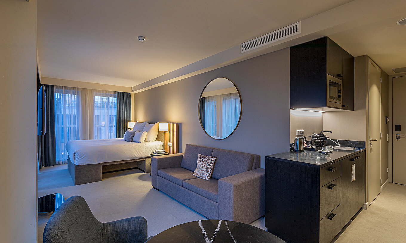 La chambre Studio Comfort du Pestana Amsterdam Riverside a un lit double, avec canapé gris et un miroir au-dessus