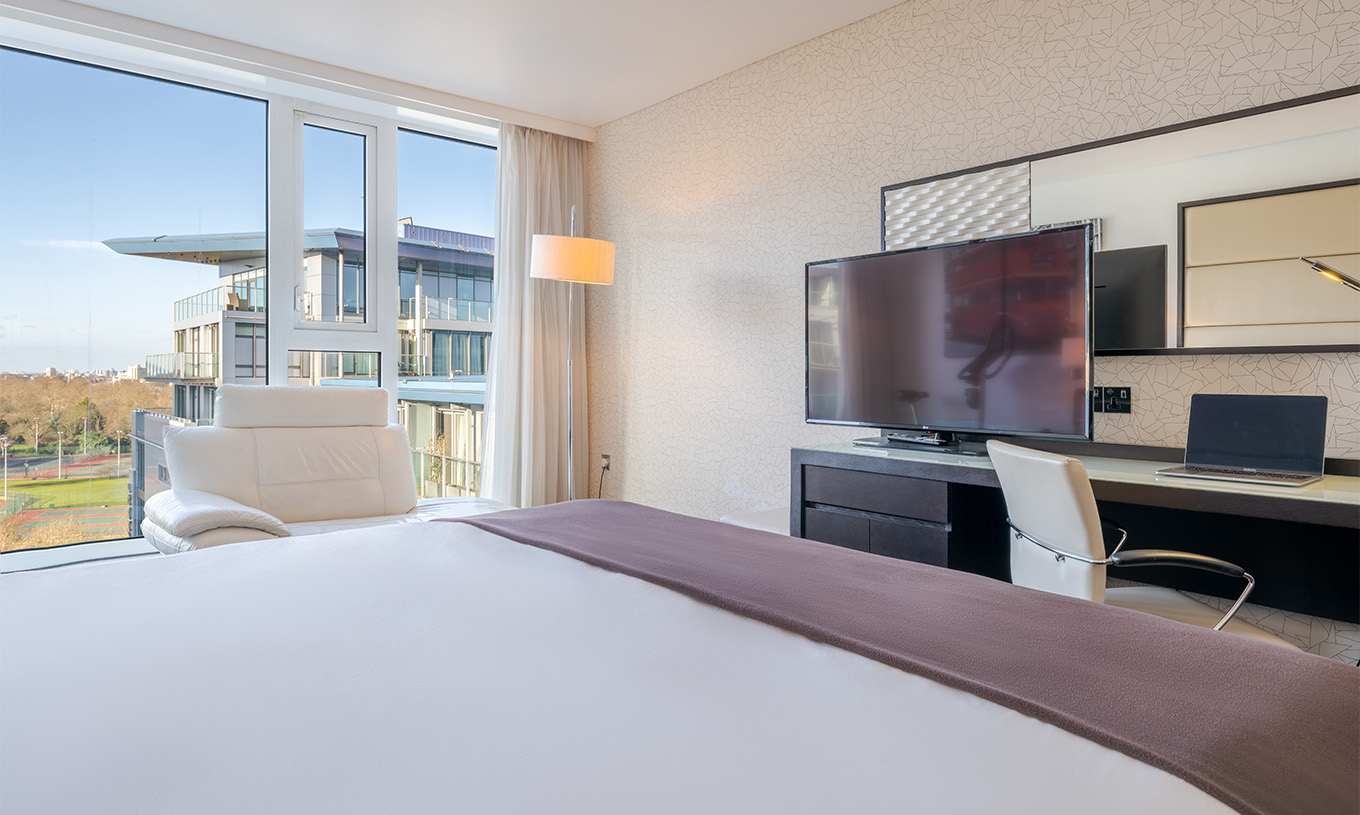 Le Deluxe Premium King du Pestana Chelsea Bridge a un lit double, un bureau avec télévision, canapé et fenêtres sur la ville