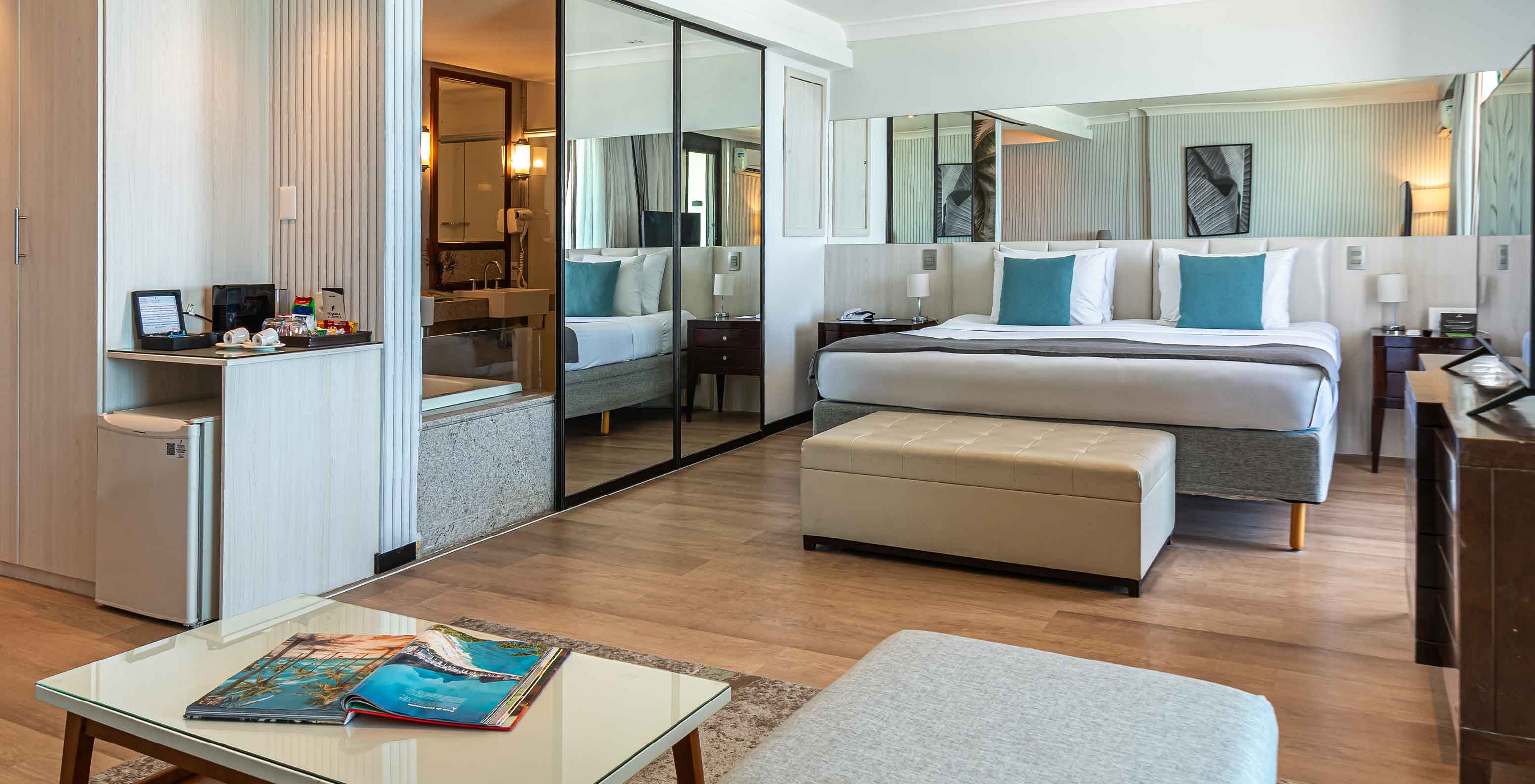 De Suite aan het strand van Pestana Rio Atlântica heeft moderne kamer met bed, spiegel en zithoek.