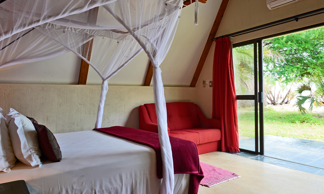 Bungalow Suite T2 van Pestana Bazaruto Lodge heeft bed met hemelbed en uitzicht op tuin en een dubbele bank aan de zijkant