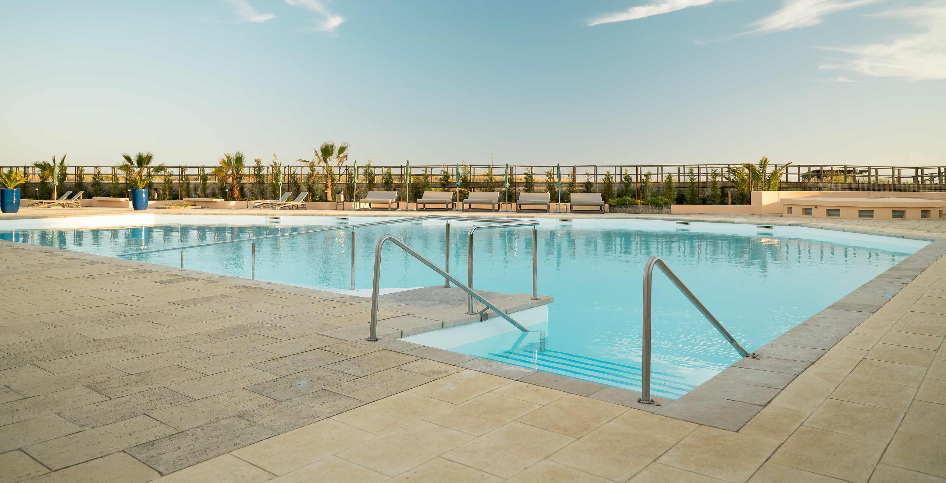 Buitenzwembad van Pestana Alvor Beach Villas, comfortabele ligstoelen, palmbomen en groene vegetatie