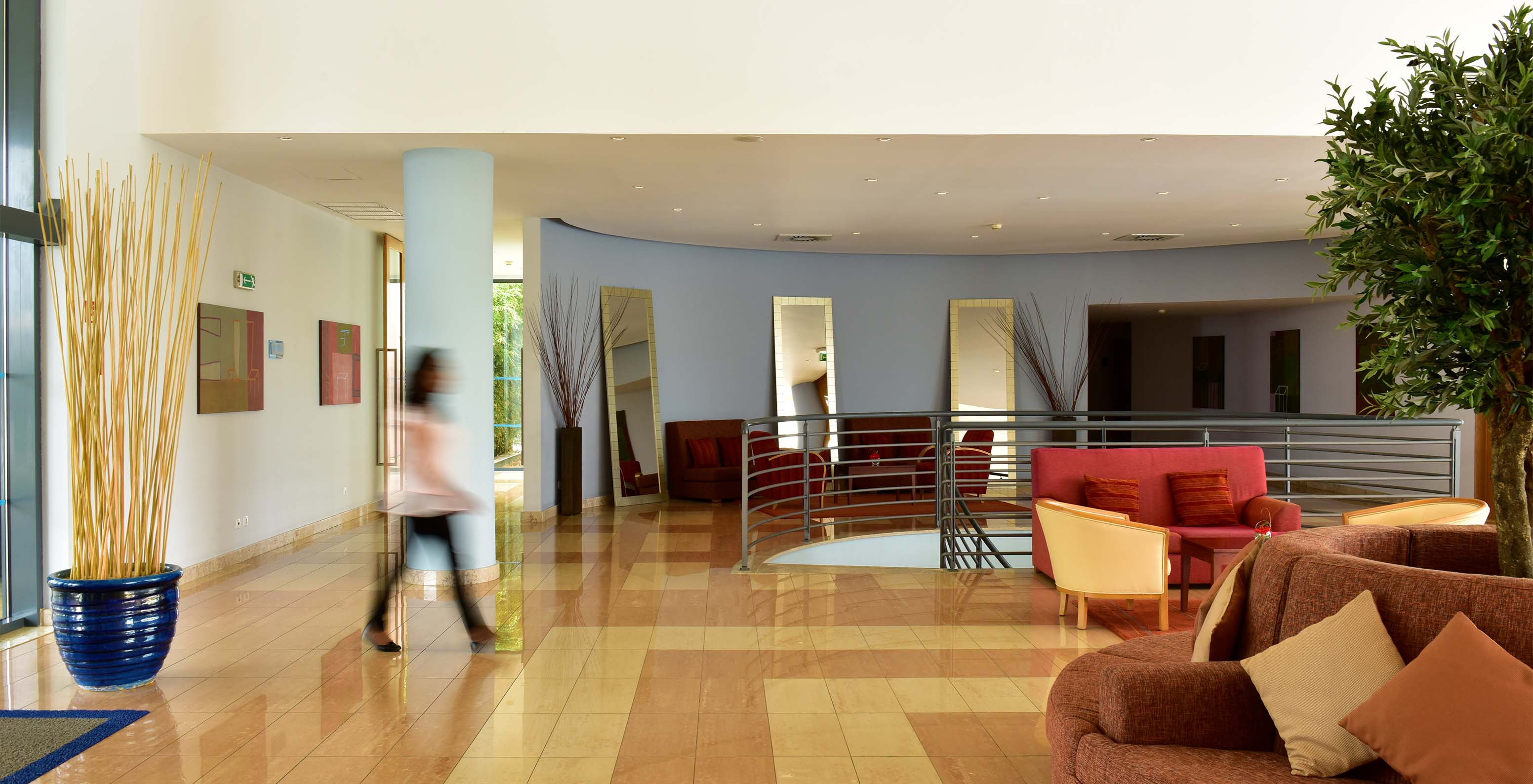 Entree van het hotel met rode en oranje banken, met metalen trappen en een vrouw die loopt