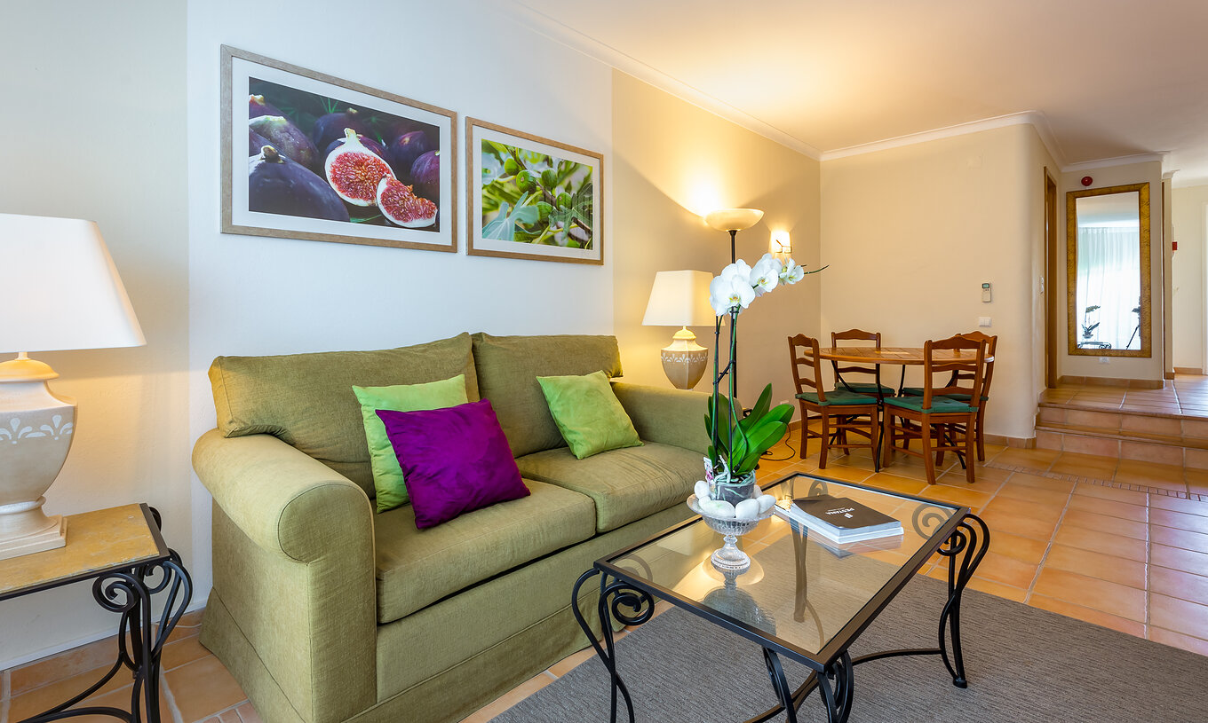 Het Appartement T2 Standard van Pestana Palm Gardens heeft een woonkamer met bank en kussens, een ronde tafel en schilderijen