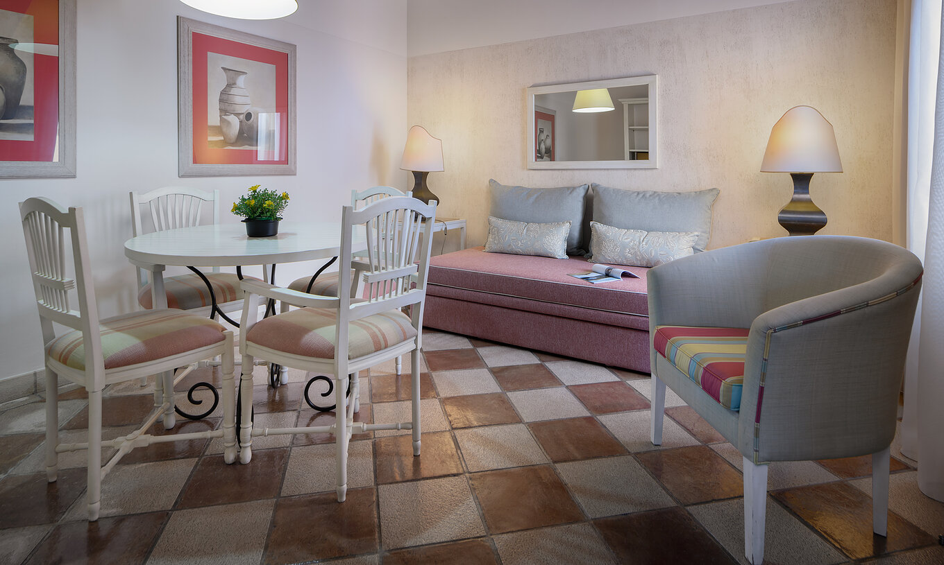 De Suite Tuinzicht van Pestana Vila Sol - Vilamoura heeft een kamer met een bank, tafel, stoelen en een spiegel aan de muur