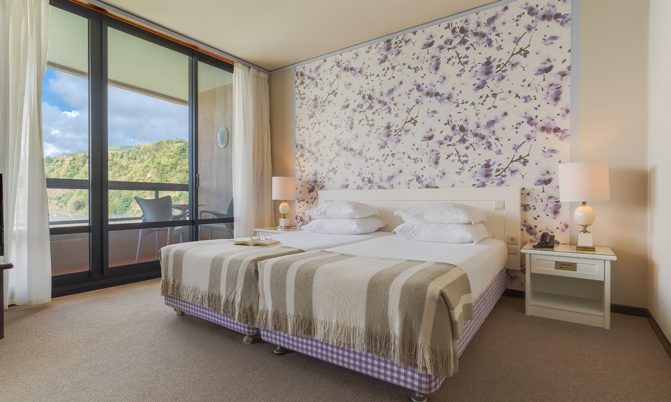 In Junior Suite Zeezicht van Pestana Bahia Praia staan de bedden naast het balkon met uitzicht op tuinen en zee