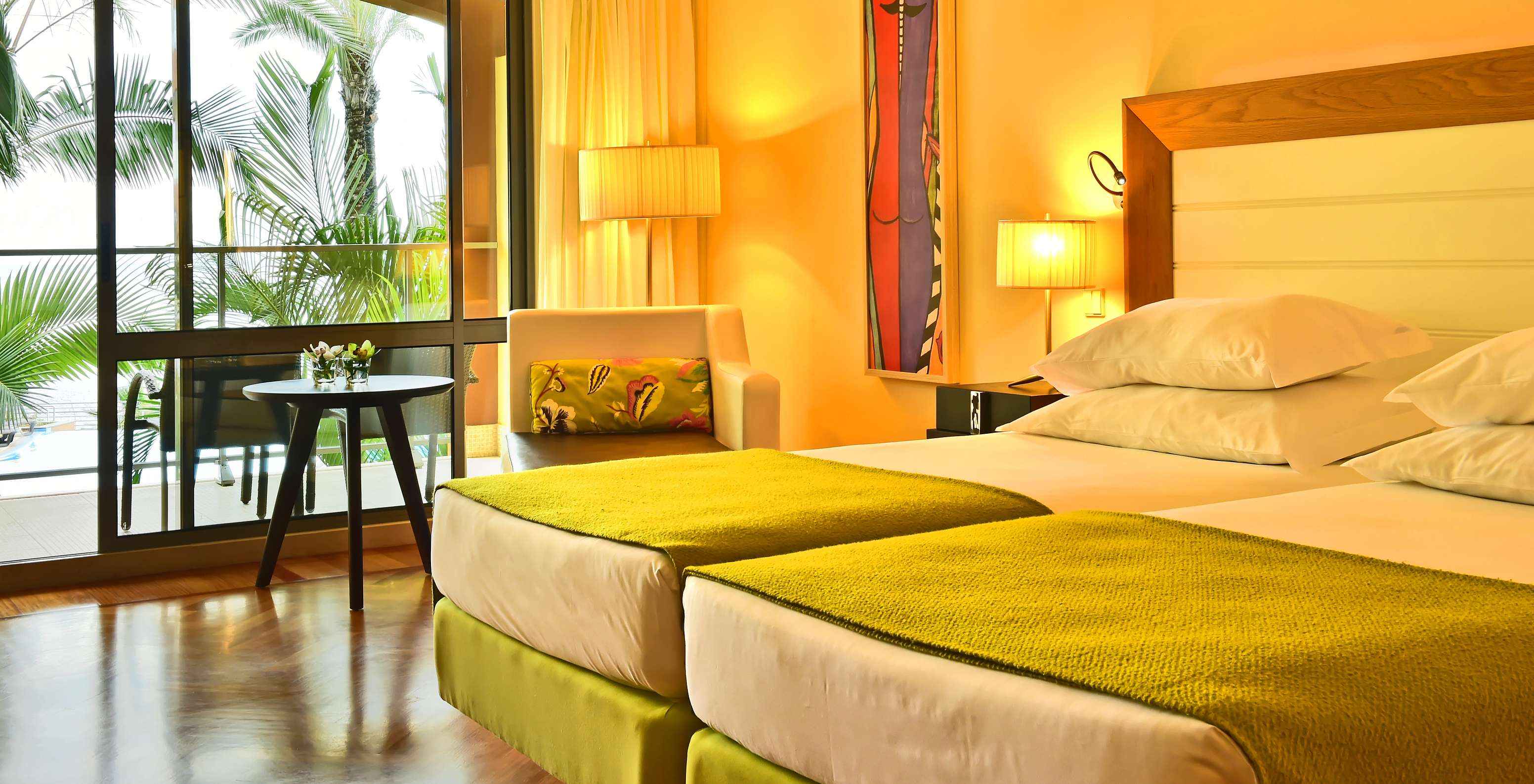 De Vista Zwembad Kamer van Pestana Promenade heeft twee bedden met een groene dekbed en een groot raam naar het balkon