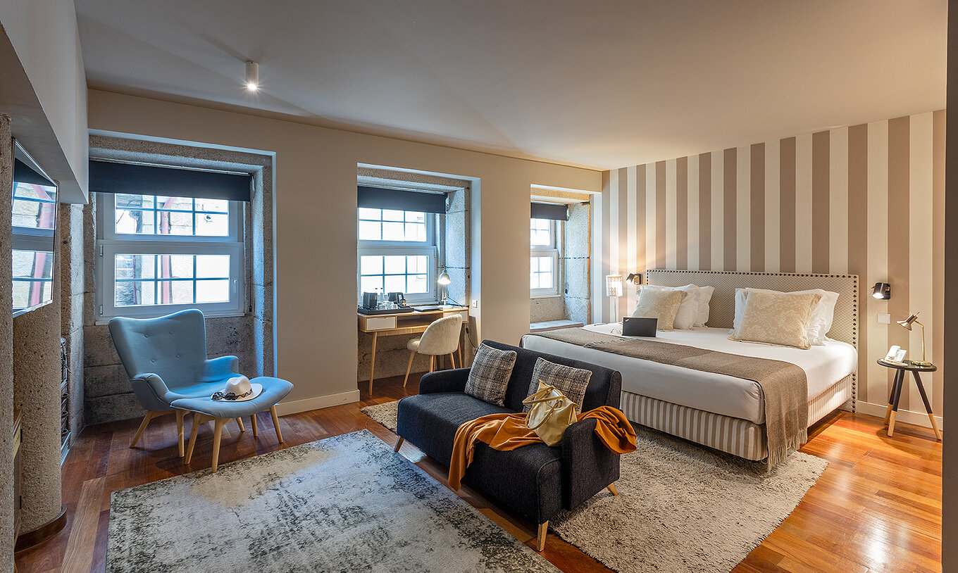 De Heritage Suite van het Pestana Vintage Porto heeft een tweepersoonsbed, twee banken op tapijten en meerdere ramen