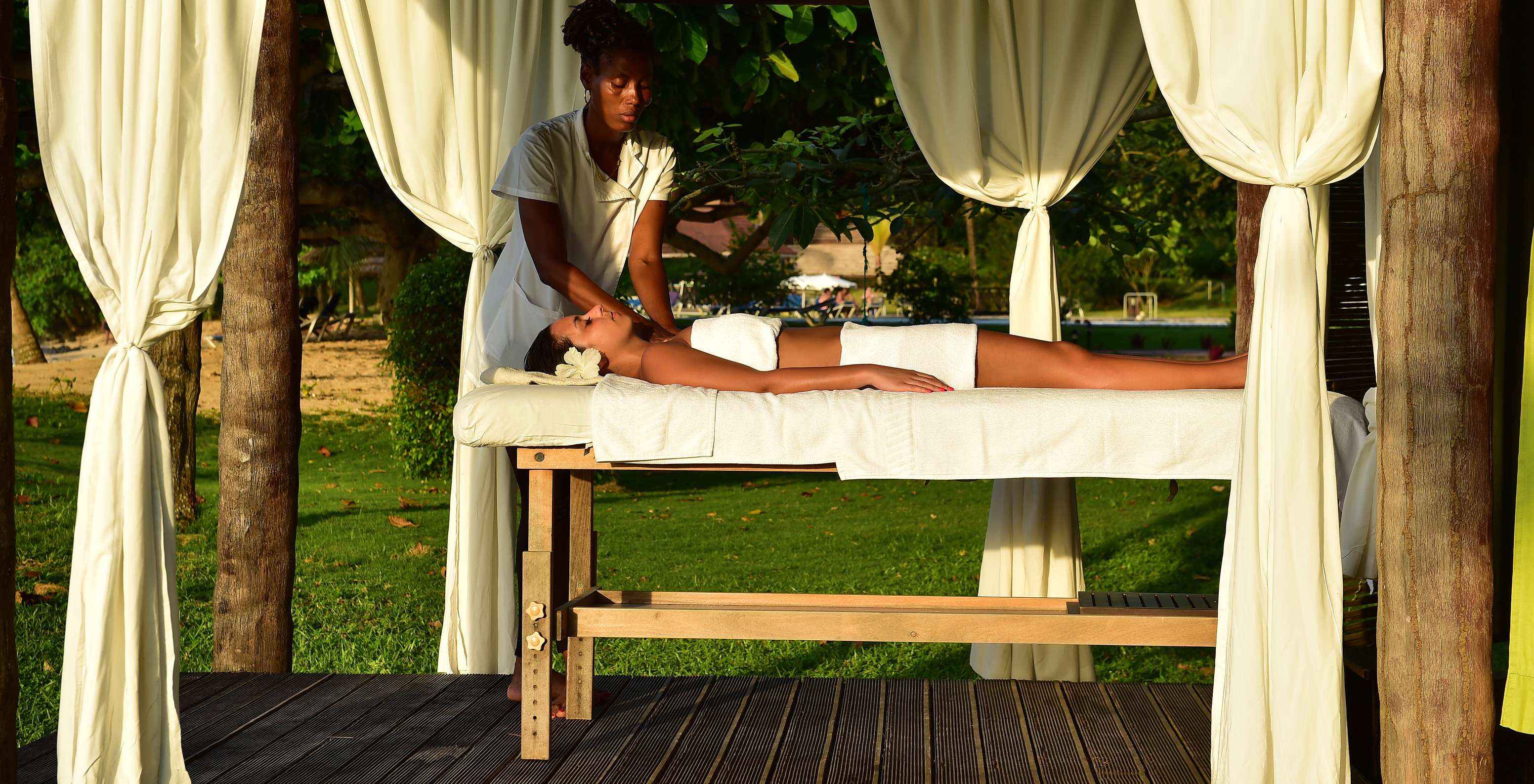Meisje met bloem in het haar krijgt een massage in de openlucht bij vakantiehotel, met zwembad en spa, aan het strand