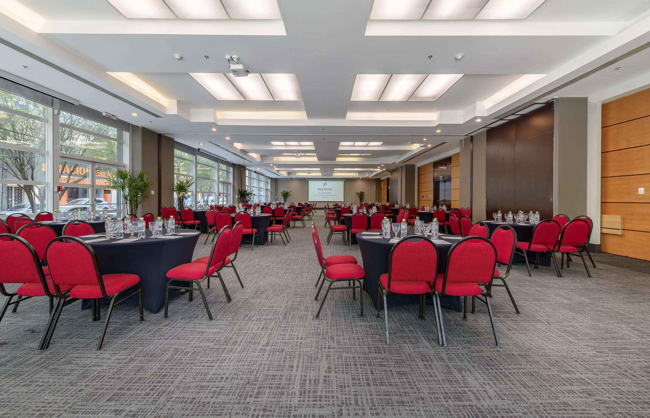 Vergader- of conferentieruimte, met verschillende ronde tafels, rode stoelen, glazen en waterflessen