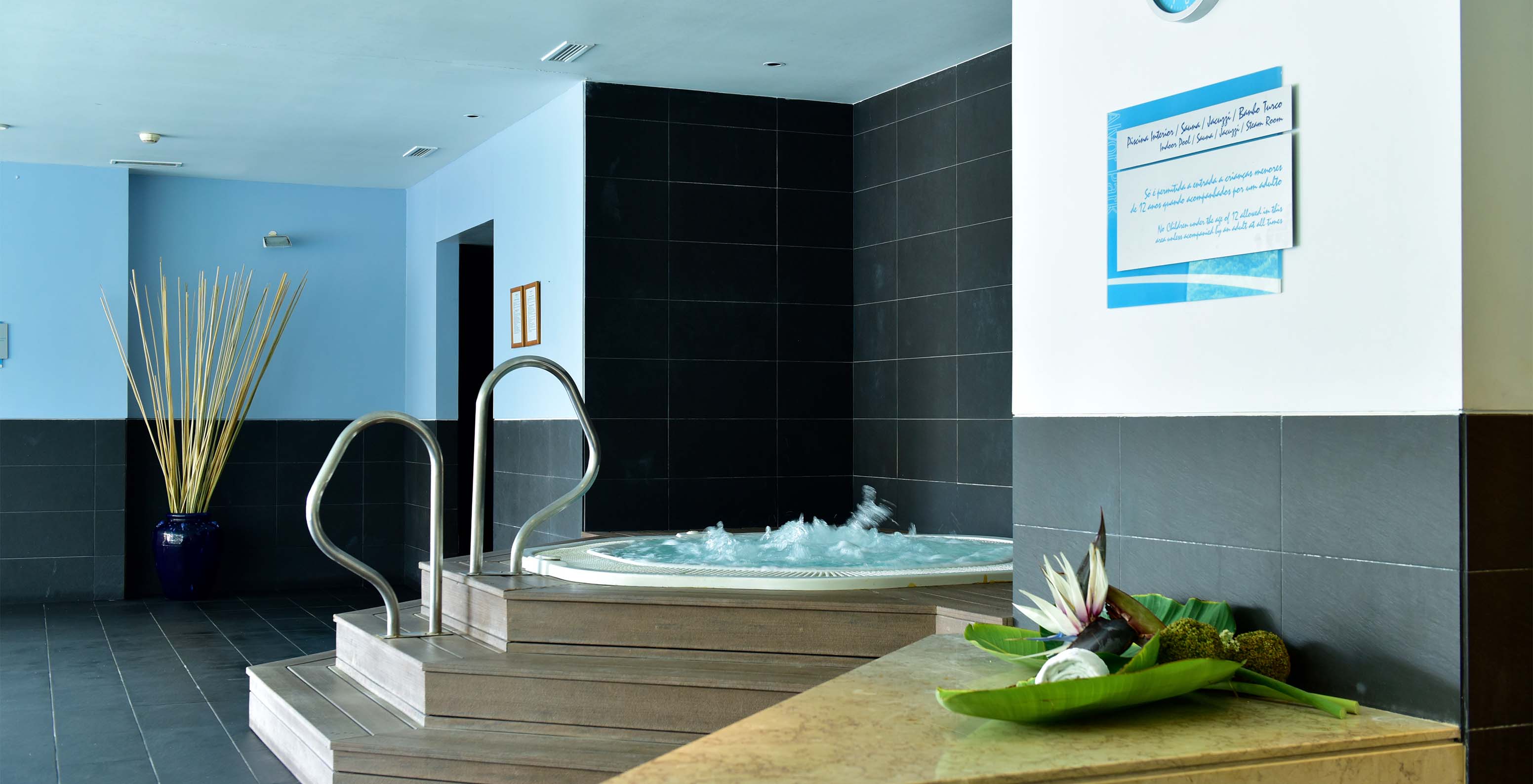 Jacuzzi com escadas em madeira e apoios metálicos, com chão de pedra preto e relógio de parede