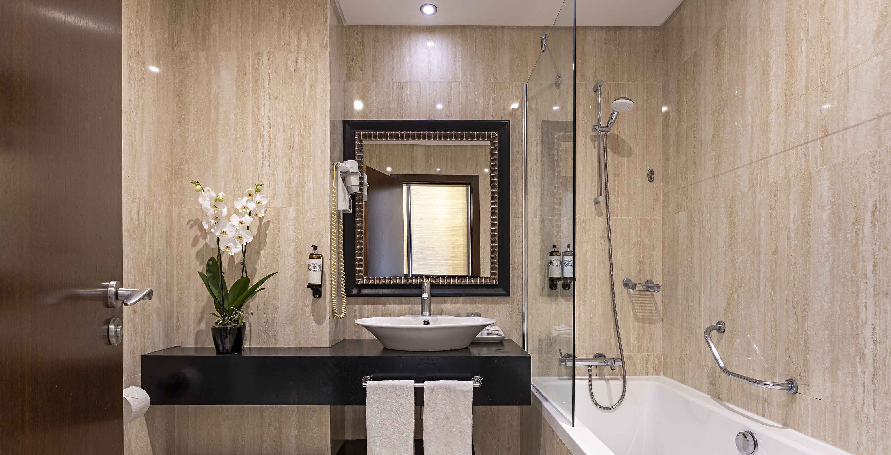 A Cliff Suite T2 do Pestana Alvor Praia tem uma casa de banho moderna com banheira, lavatório, sanita, um espelho e flores