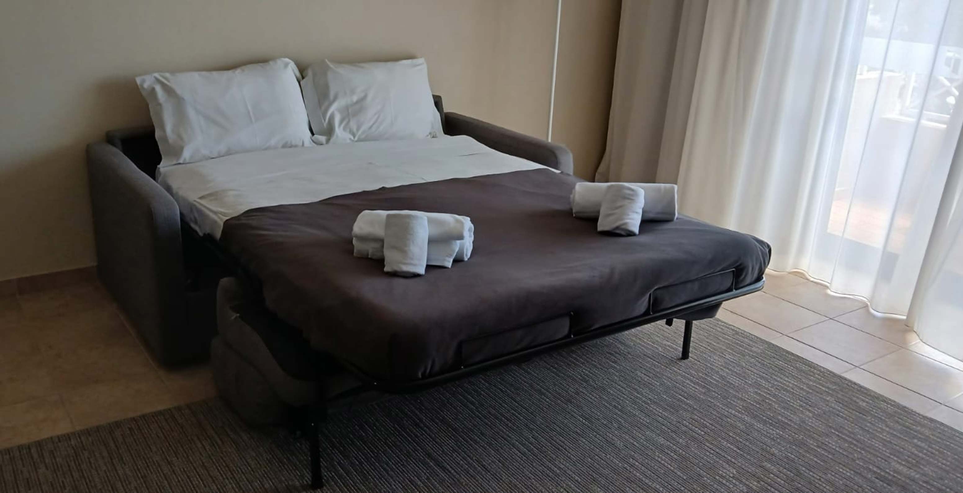 O Studio do Pestana Gramacho Residences tem um sofá-cama aberto com lençóis brancos e toalhas dobradas.