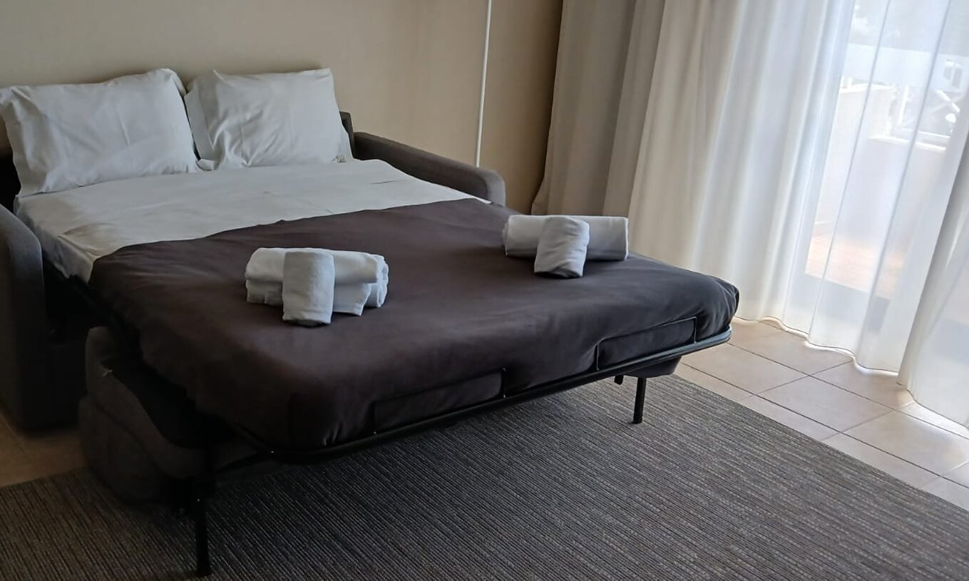 O Studio do Pestana Gramacho Residences tem um sofá-cama aberto com lençóis brancos e toalhas dobradas.