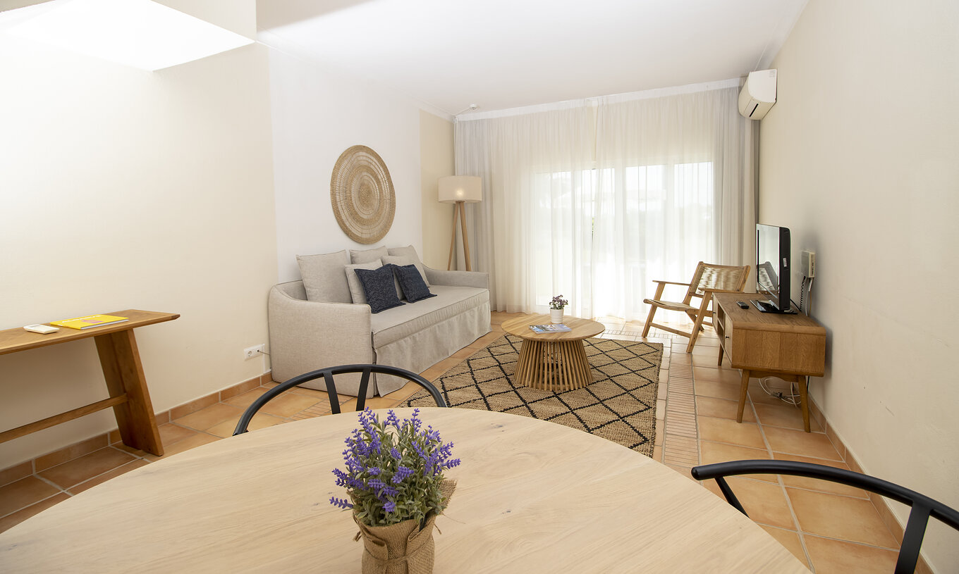 O Apartamento T2 Superior do Pestana Palm Gardens tem uma sala com uma mesa redonda, sofá, televisão e janela para o jardim