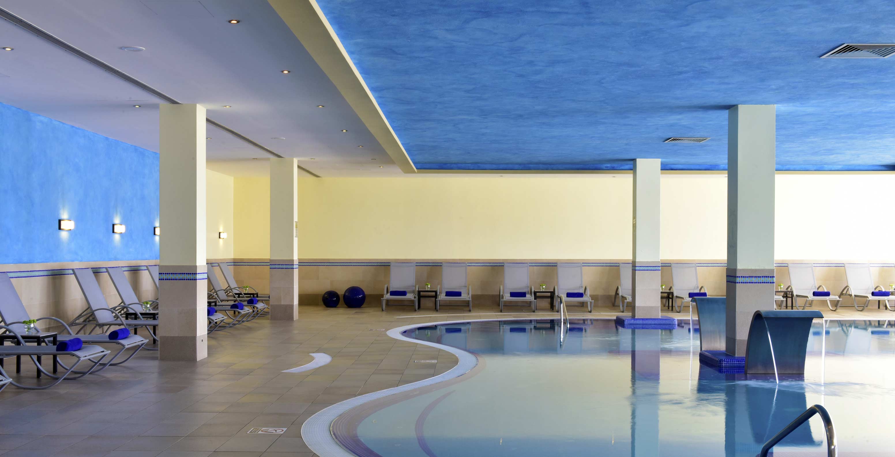 Piscina interior do Pestana Viking, com paredes em tons de azul, amarelo e ambiente calmo, com várias espreguiçadeiras