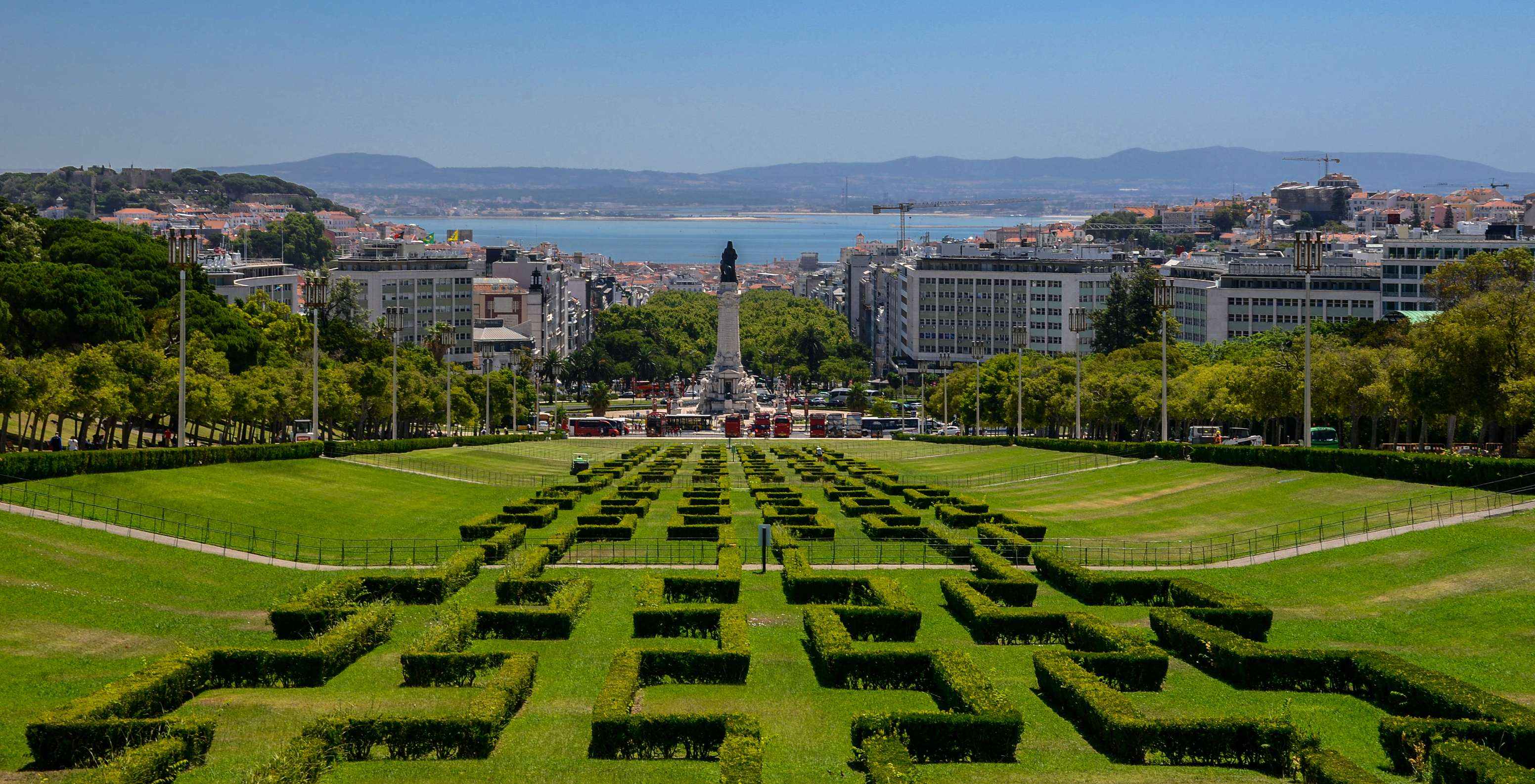 Vista de cima do Parque Eduardo VII, com os jardins verdes, edifícios, a estátua do Marquês de Pombal e o Rio Tejo