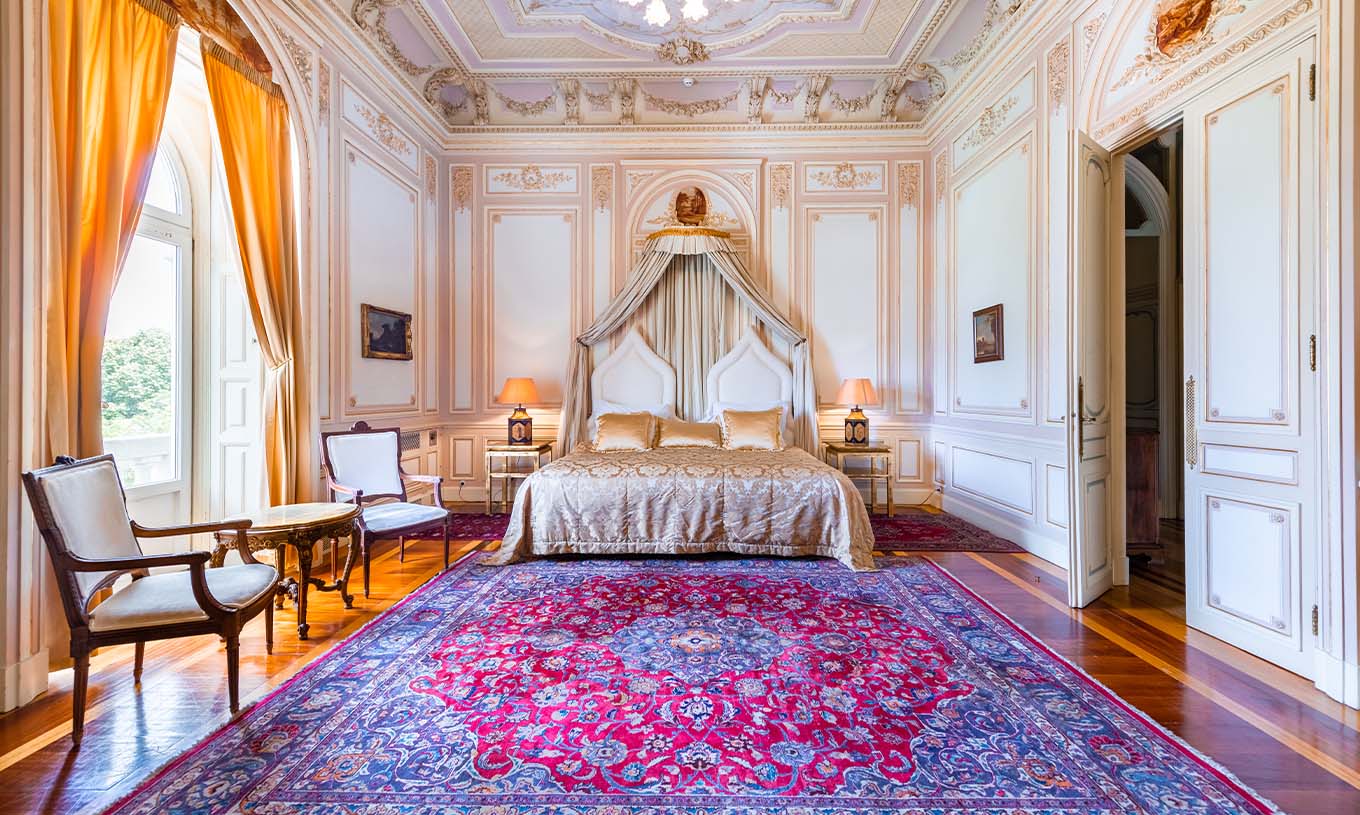 A Suite D. Carlos do Pestana Palace Lisboa tem um quarto luxuoso com cama de casal e teto com detalhes ornamentados