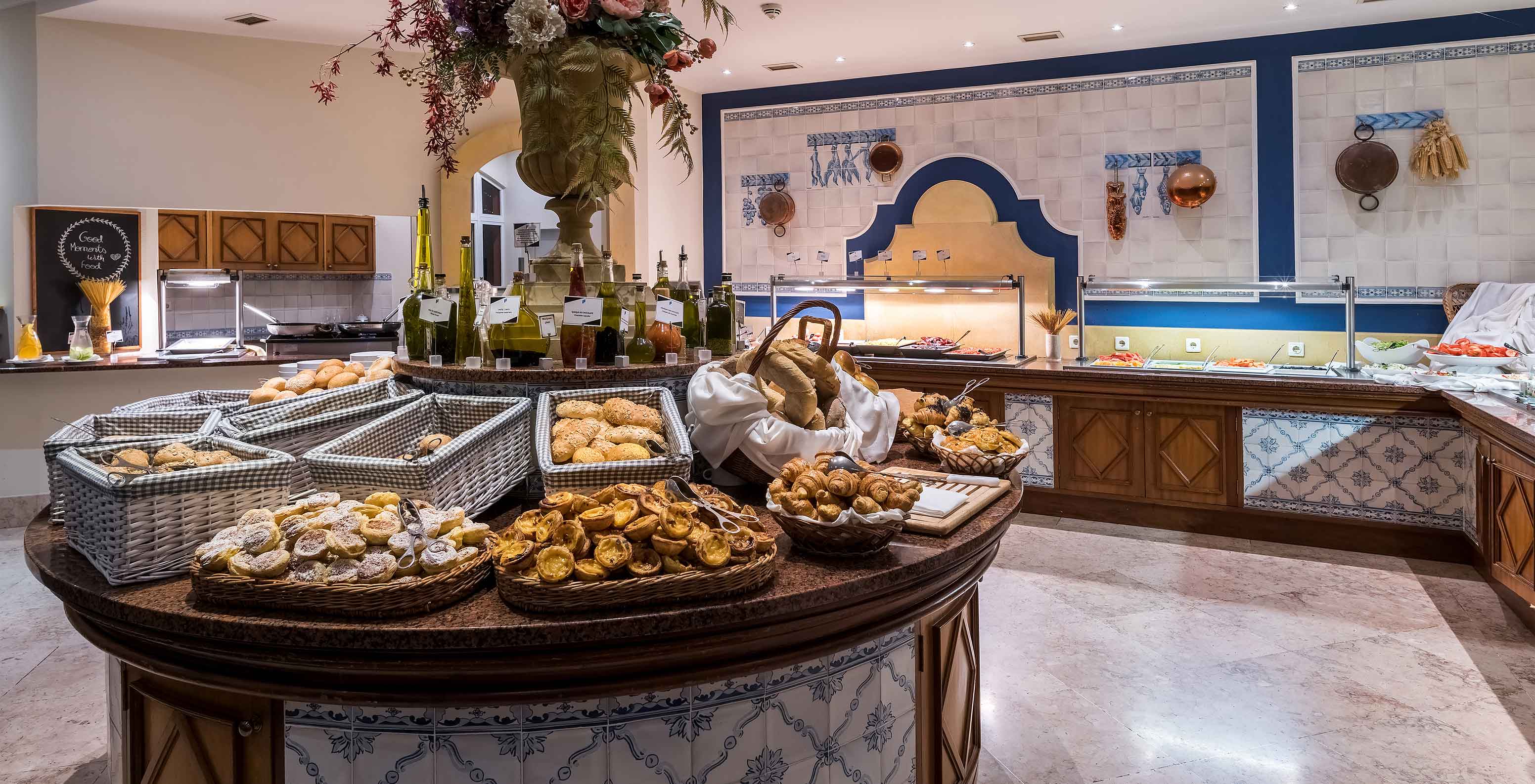 Sala pequeno almoço com vários pães e doces em cestos sobre uma mesa redonda do Pestana Village, Hotel com Piscina no Funchal