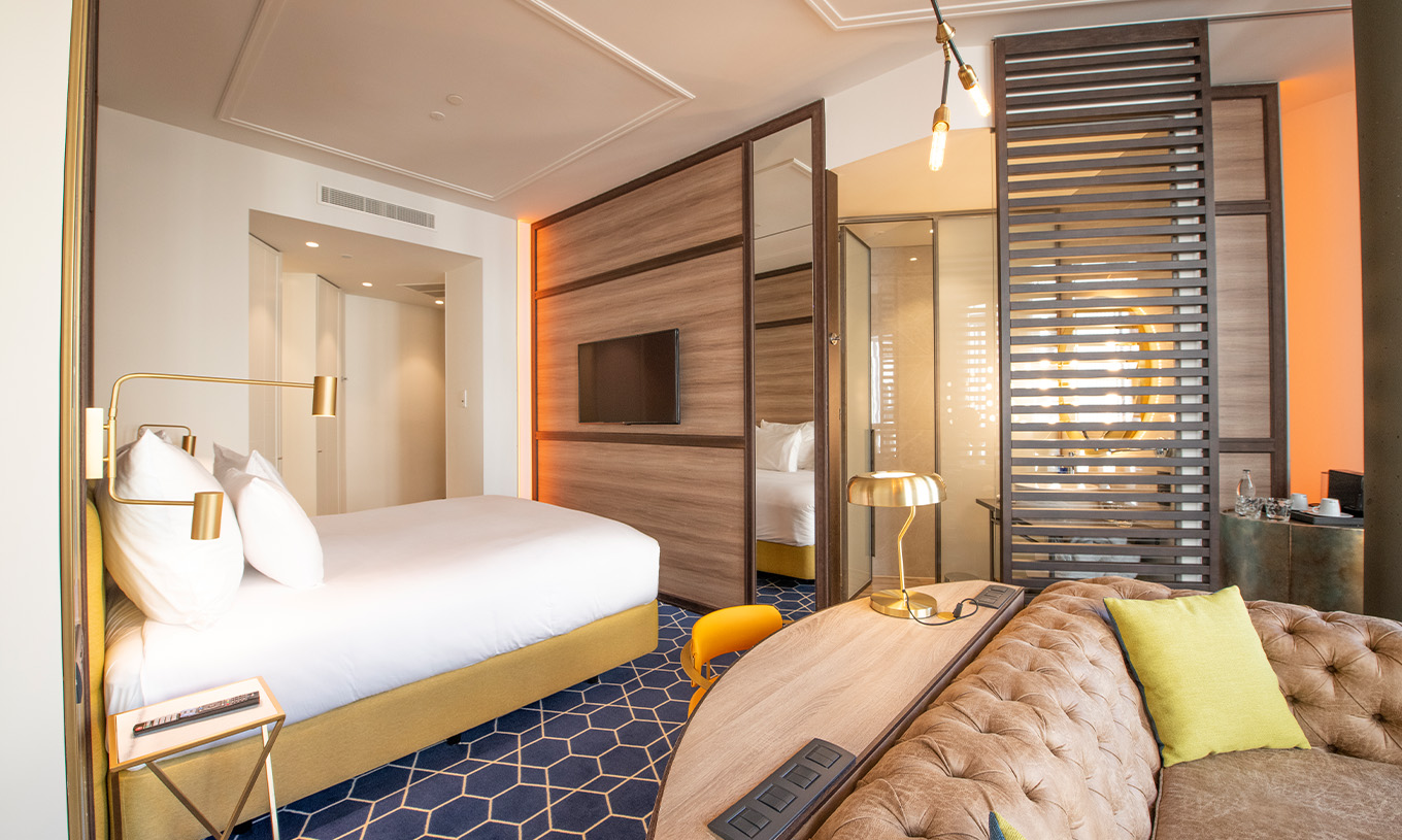 O The Fantastic 7 Room do Pestana CR7 Gran Vía Madrid tem cama de casal com sofá, secretária, espelho e divisória de madeira