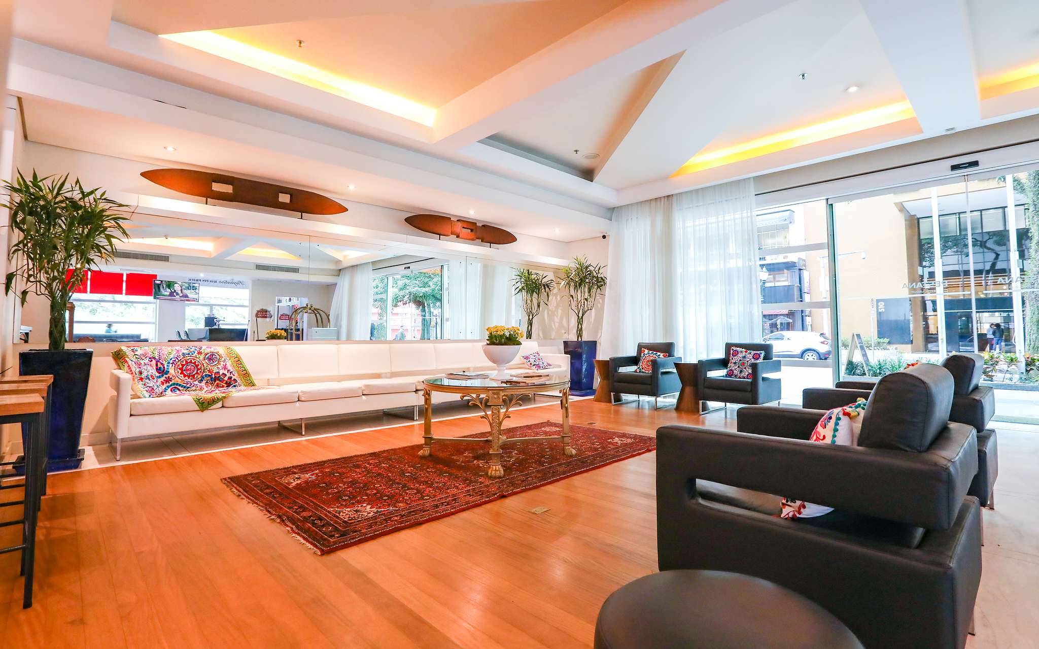 Entrada do Pestana Curitiba com 4 cadeirões e sofá branco comprido com almofadas coloridas e uma mesa de centro