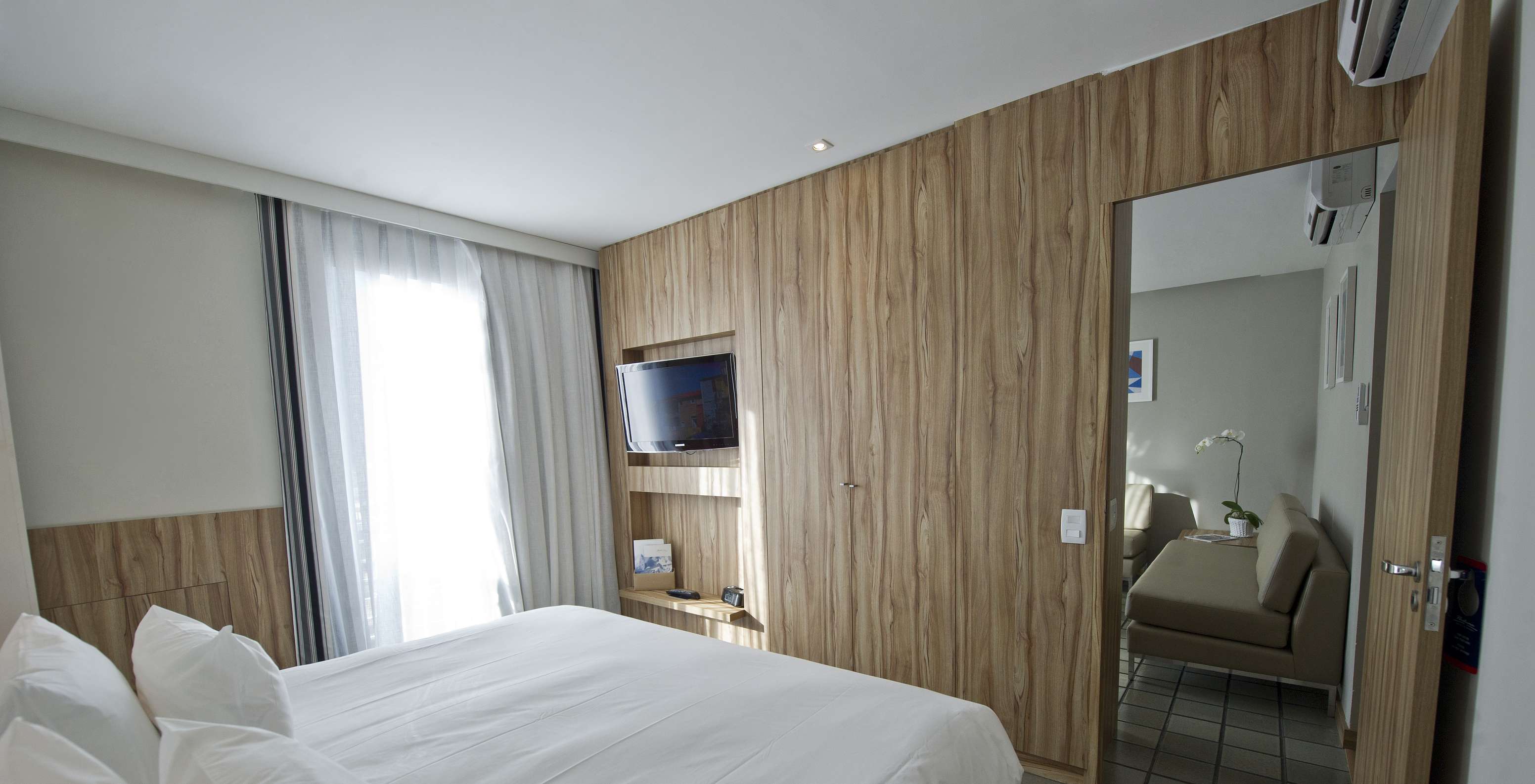 A Suite Standard do Pestana Rio Atlântica tem um quarto com cama de casal e televisão, e uma sala com sofás e ar condicionado