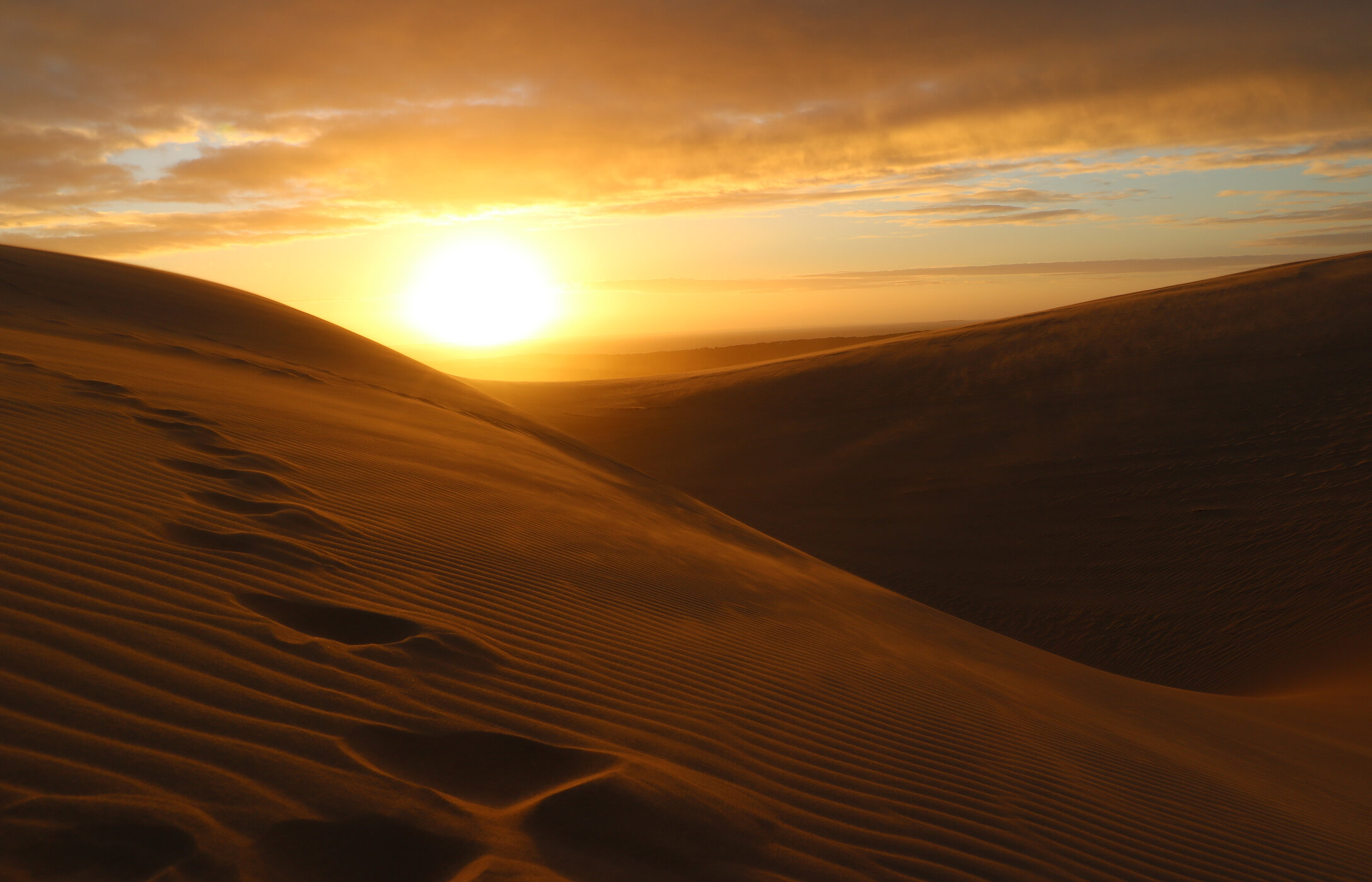 Vista panorâmica das dunas de areia em Bazaruto, com o sol a pôr-se no horizonte e um céu em tons quentes