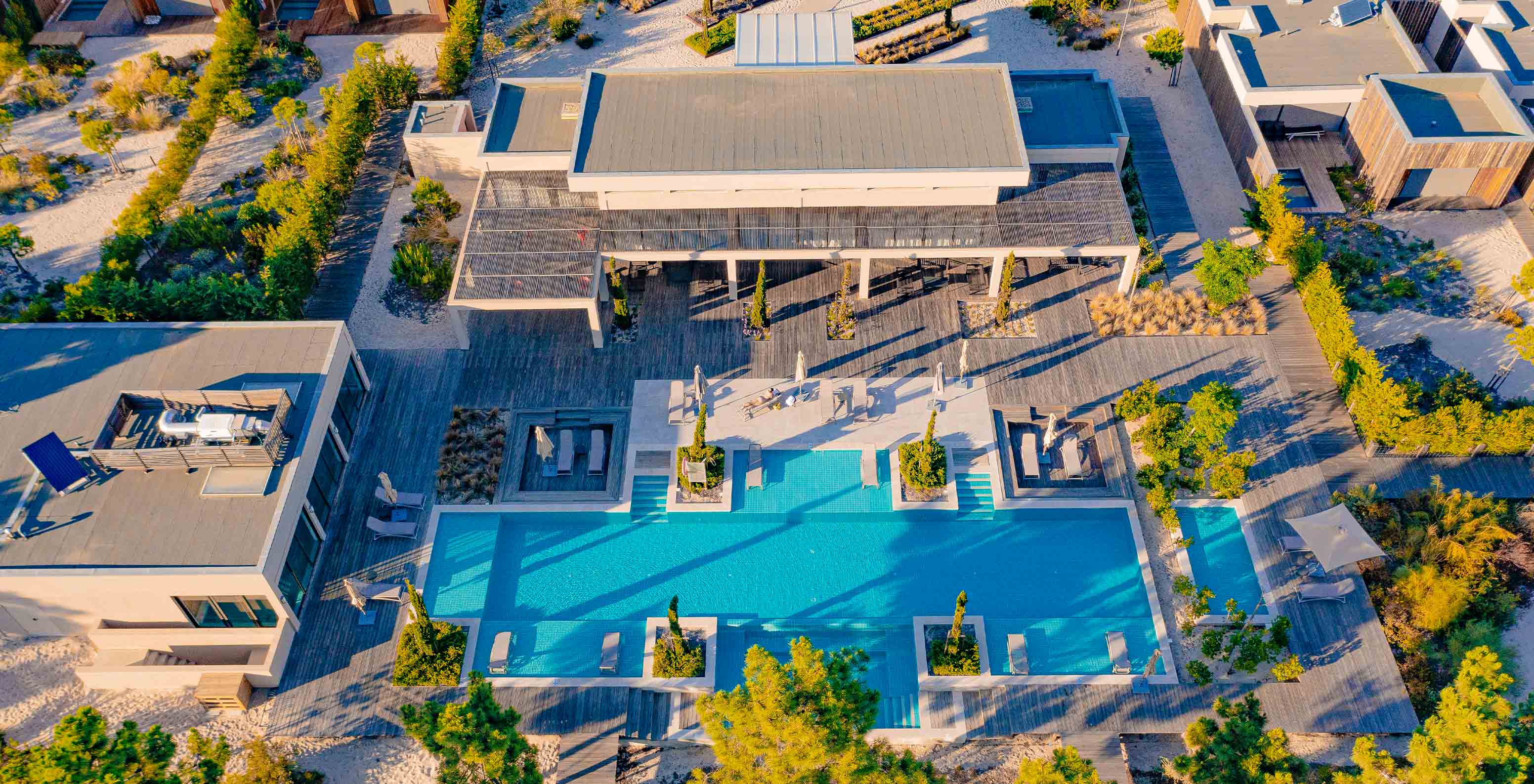 Vista aérea do Pestana Troia Eco Resort com uma grande piscina retangular cercada por espreguiçadeiras e vegetação
