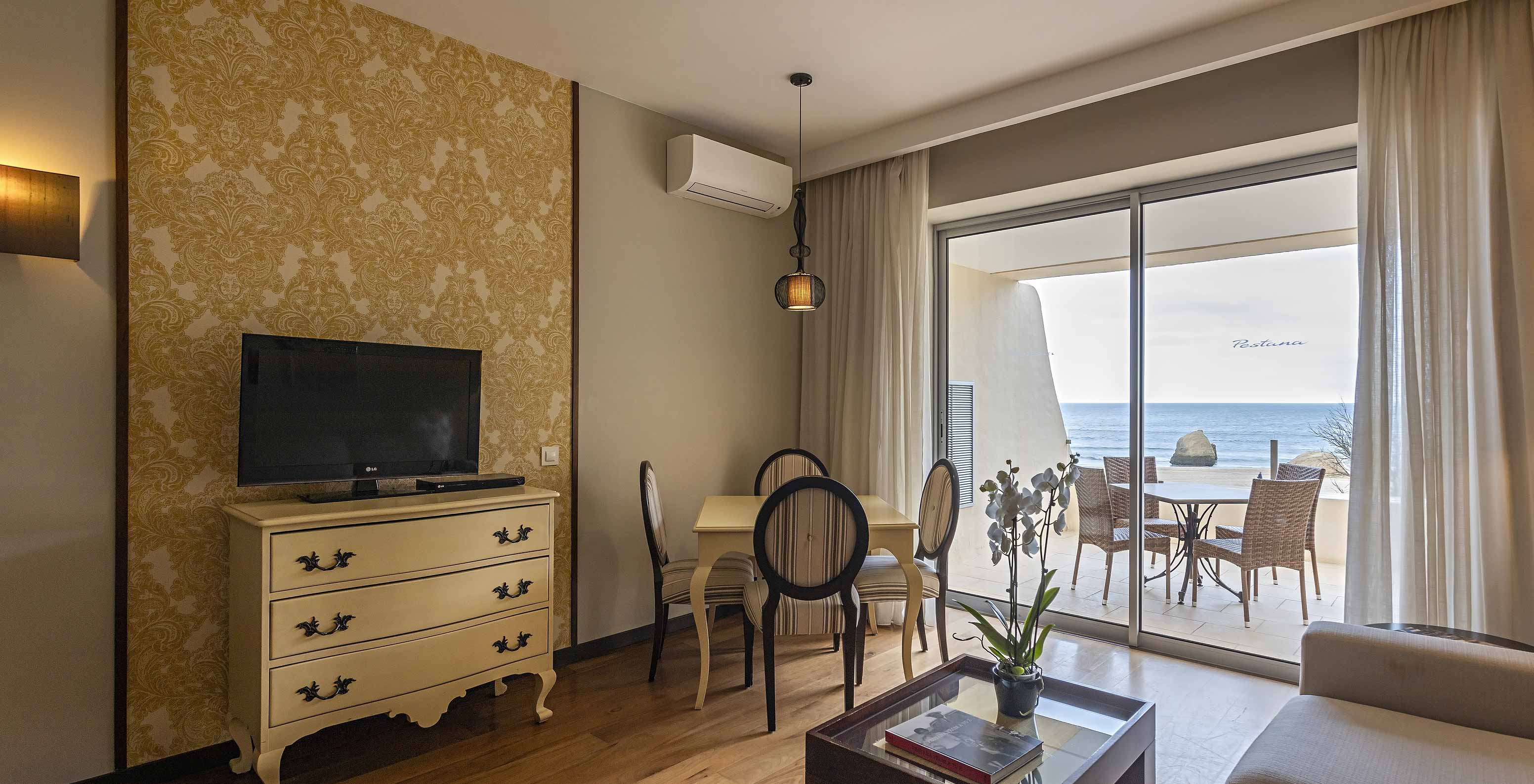 A Cliff Suite T1 do Pestana Alvor Praia tem uma sala com televisão e uma varanda com uma mesa, cadeiras e vista para o mar