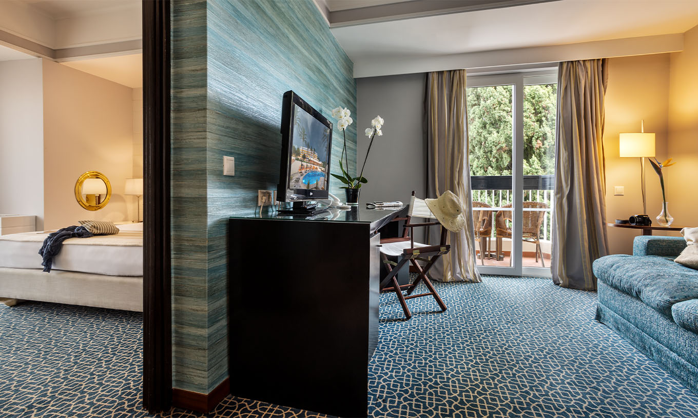 A Suite Vista Jardim do Pestana Alvor Praia tem uma divisão entre a sala com sofá, secretária e televisão e o quarto com cama