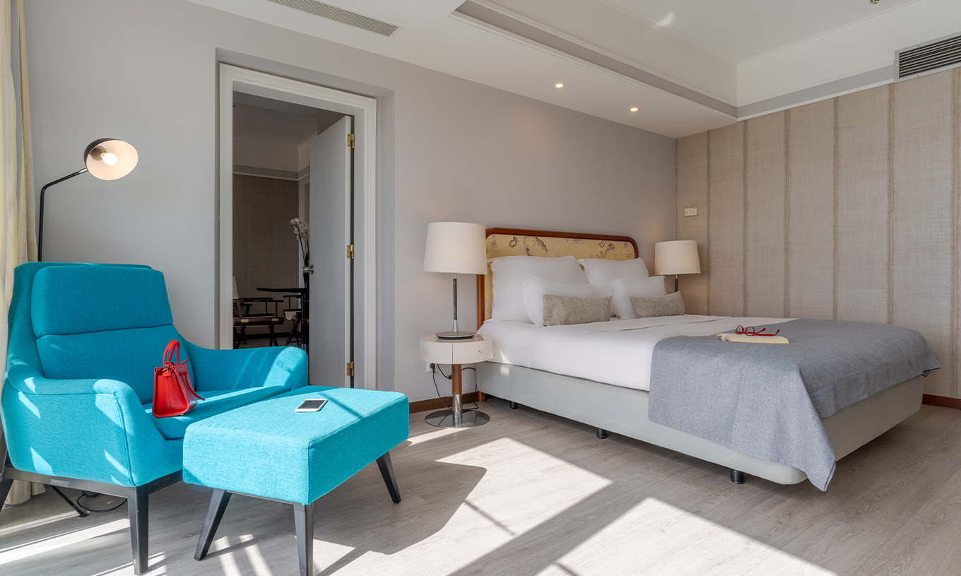 A Suite Vista Mar do Pestana Alvor Praia tem cama de casal com cadeirão e pousa-pés azuis, com candeeiros e chão de madeira