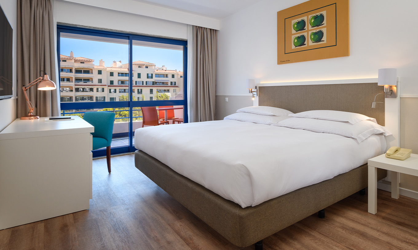 A Suite Deluxe do Pestana Cascais conta com cama de casal, secretária, e um quadro pintado na parede