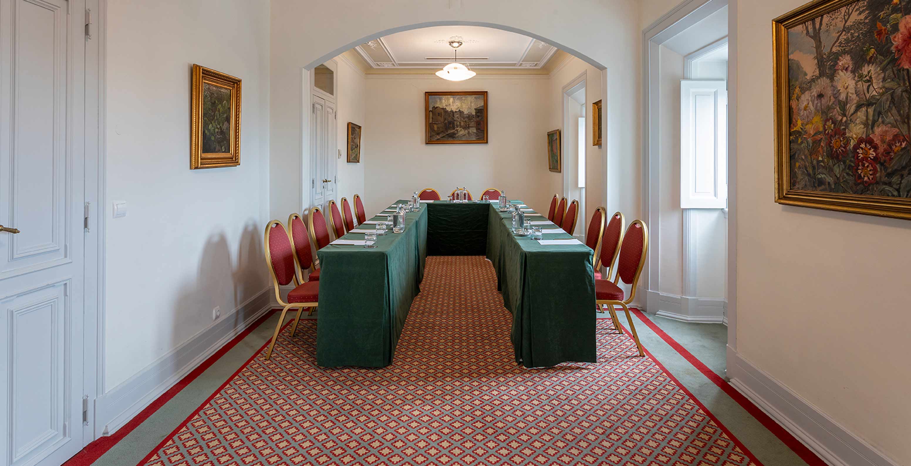 O Pestana Palace Lisboa tem uma sala de reuniões com uma mesa verde em "U" e várias cadeiras vermelhas