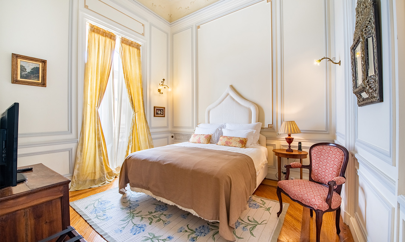 A Suite D. Amélia do Pestana Palace Lisboa tem uma cama de casal, mesa de cabeceira em madeira, uma cadeira, tapete e janela